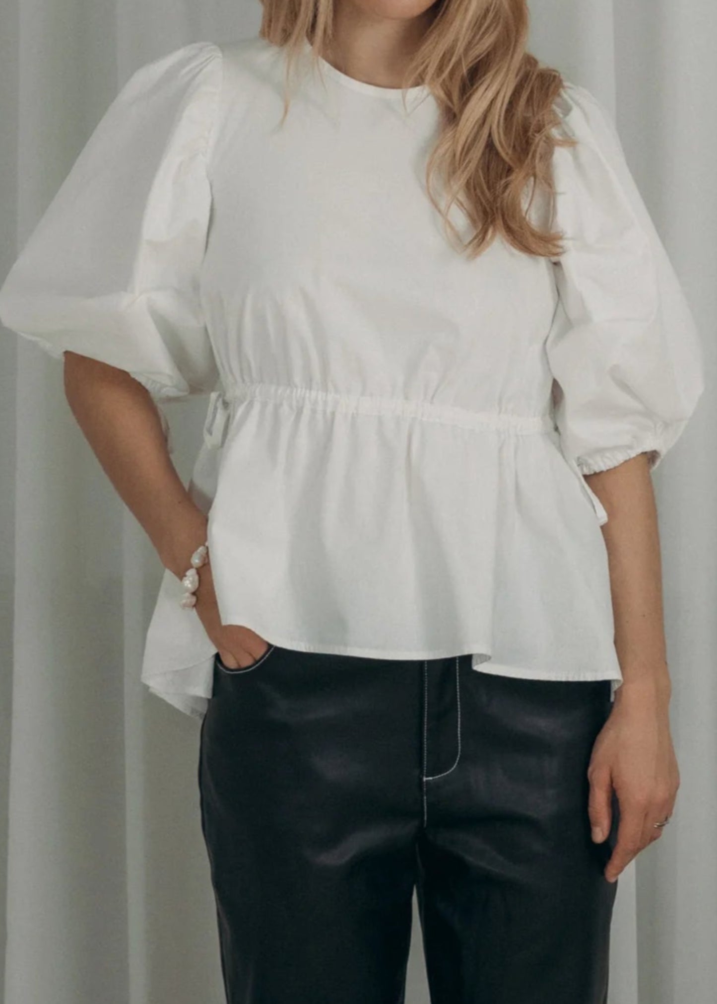 Woman wearing a white blouse with puffed sleeves and black pants against a plain background