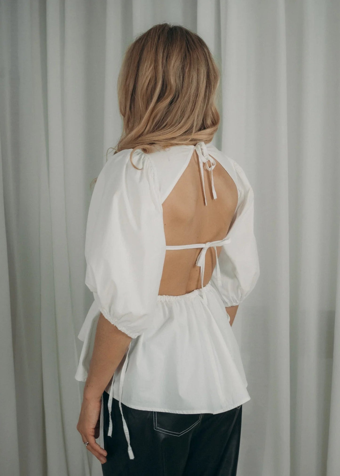 Person wearing a white blouse with cut-out design against a plain background