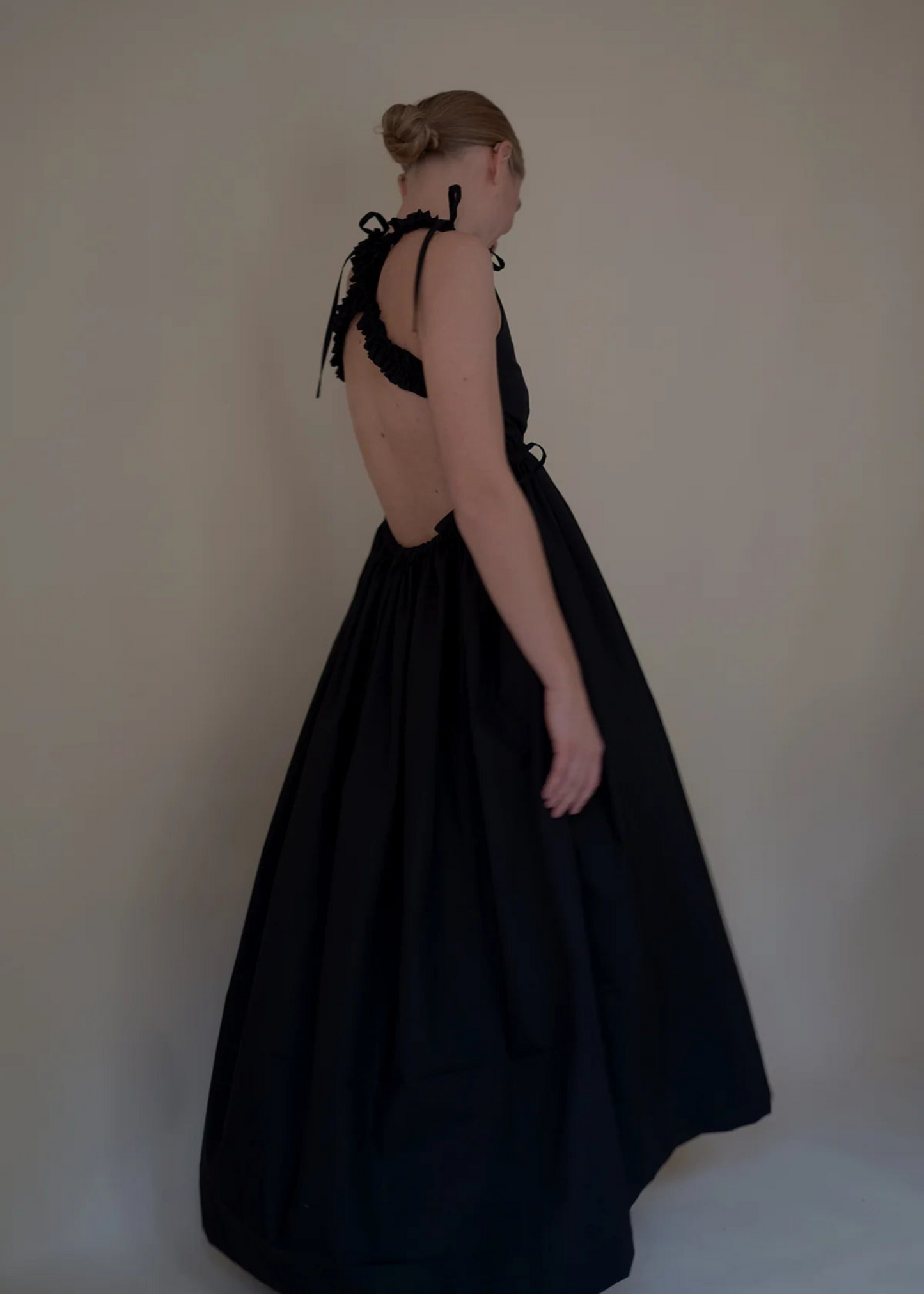 Woman wearing a black dress with open back against a plain background