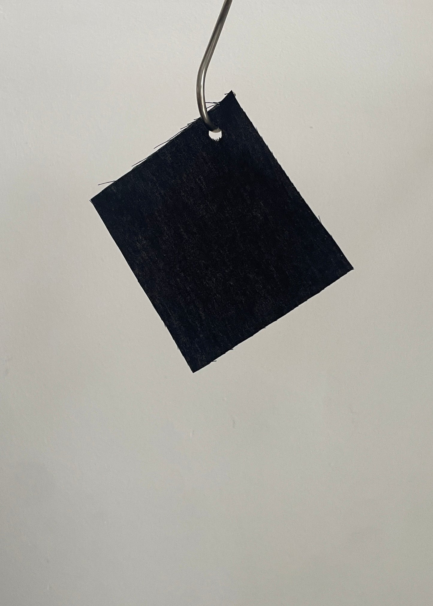 Black square fabric sample hanging on a metal rod against a light gray background
