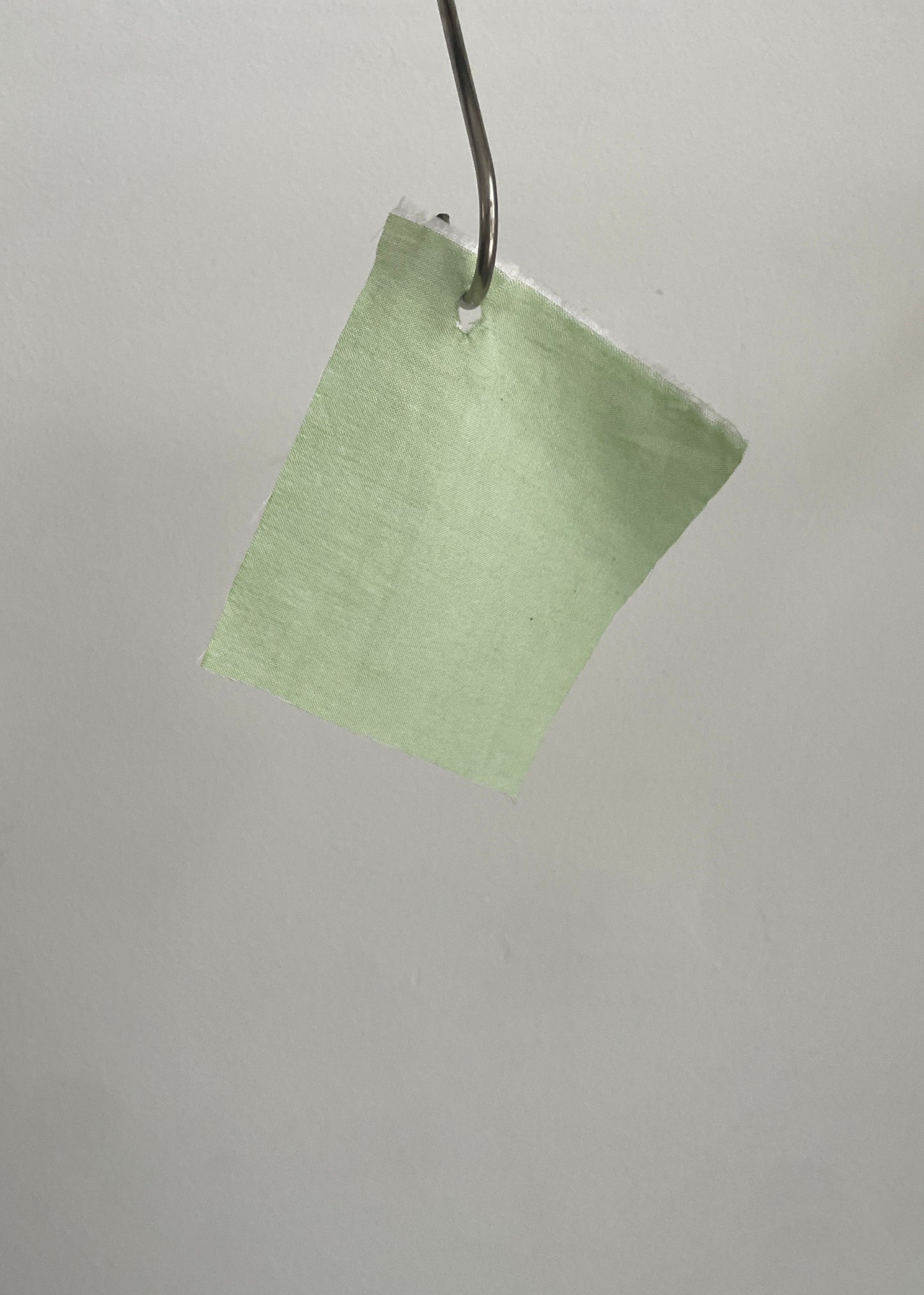 Green square fabric sample hanging on a metal rod against a gray background