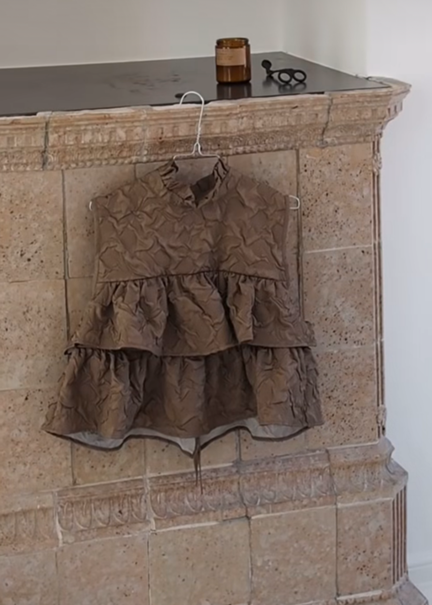 Brown dress hanging on a stone fireplace with a white background