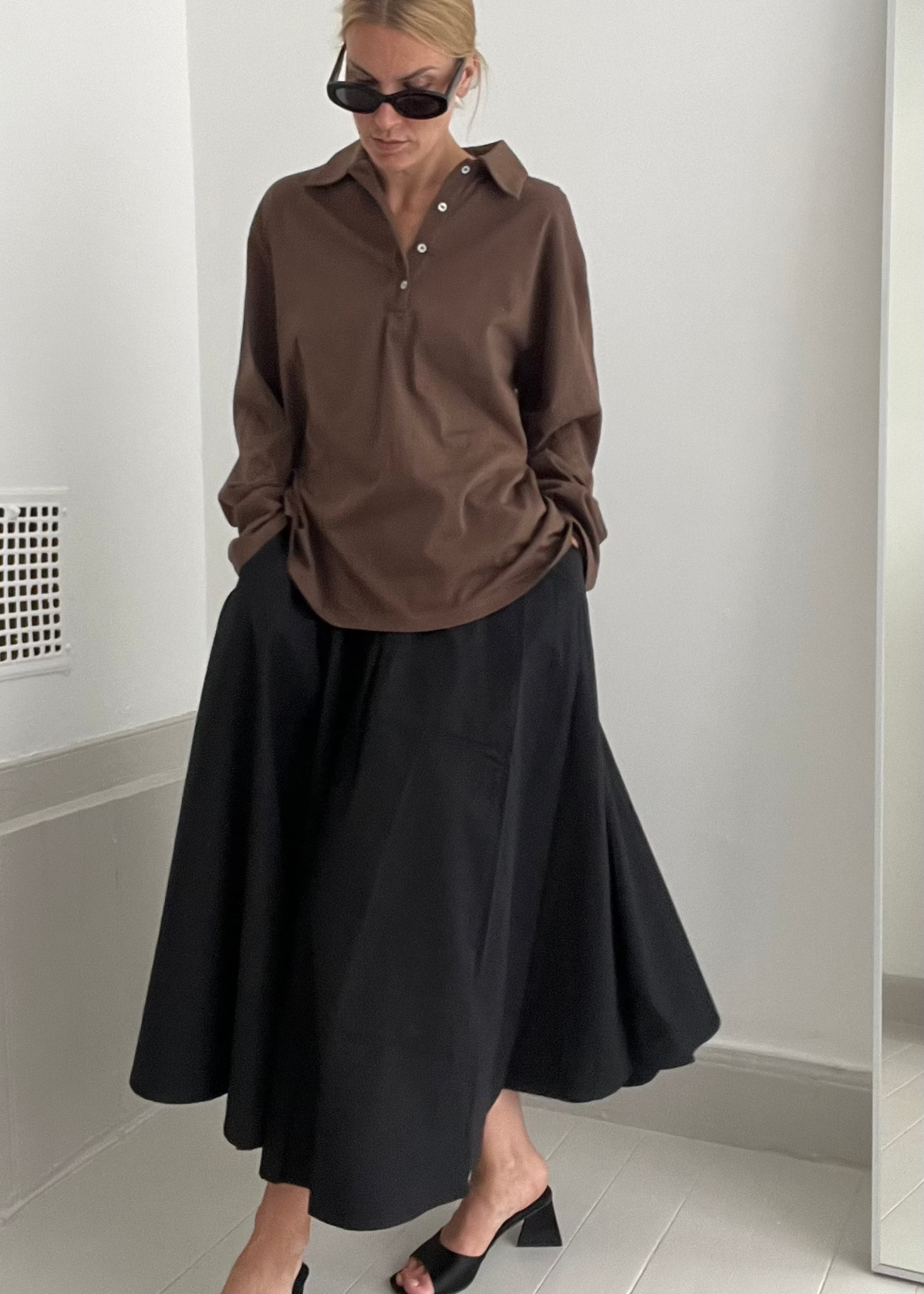 Person wearing a brown shirt and black skirt in a minimalistic setting