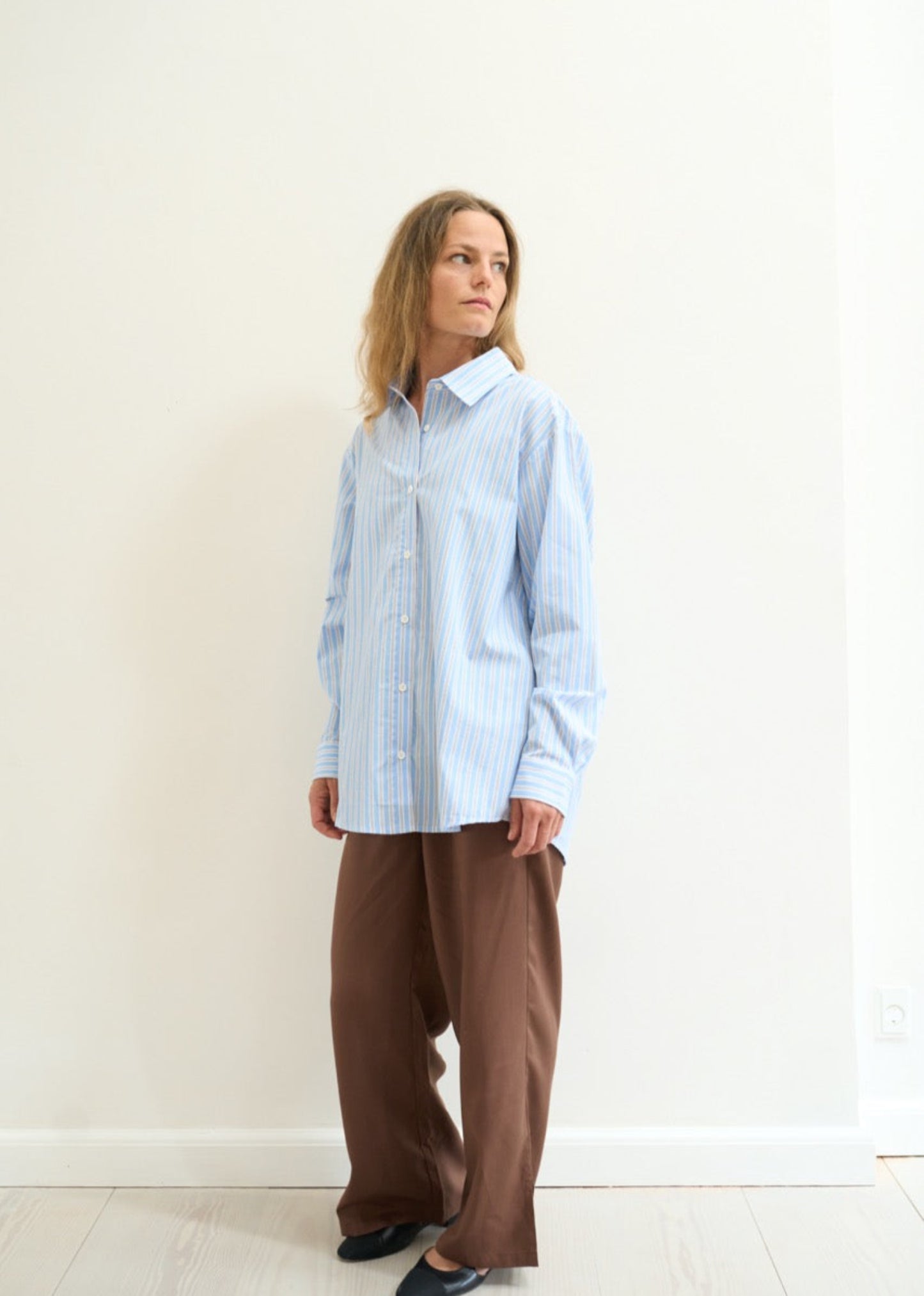 Person wearing a light blue checkered shirt and brown pants against a white background
