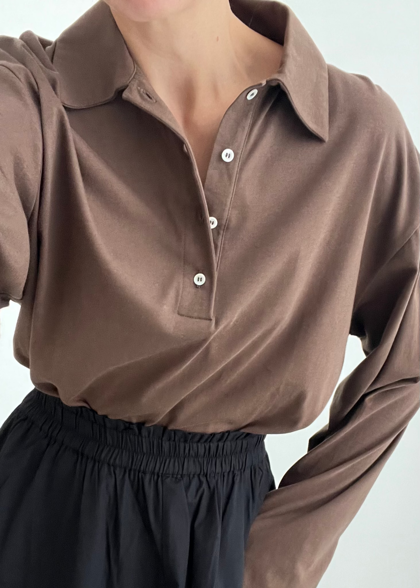 Person wearing a brown long-sleeve shirt with a collar against a white background