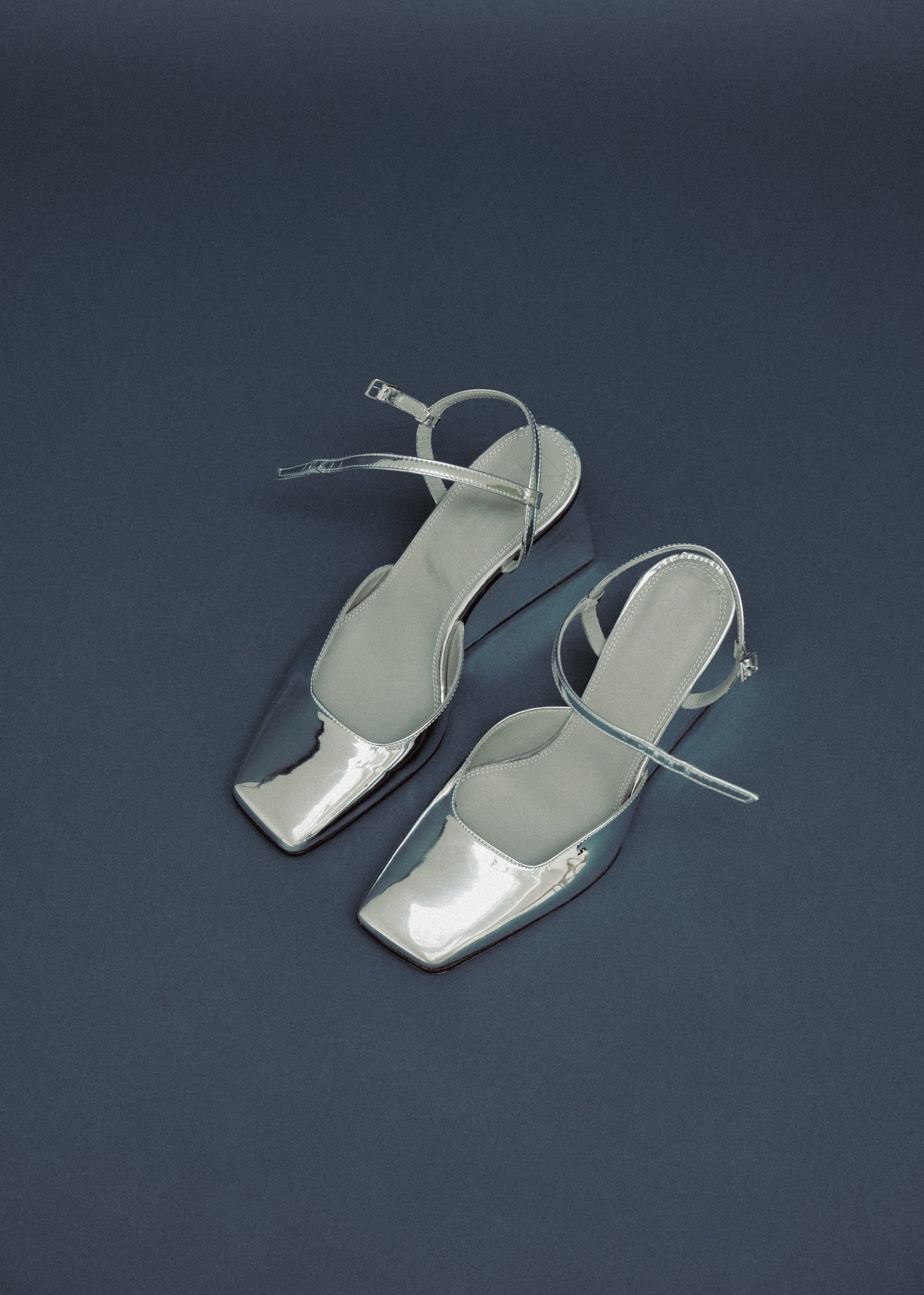 Pair of silver high-heeled sandals on a dark blue background