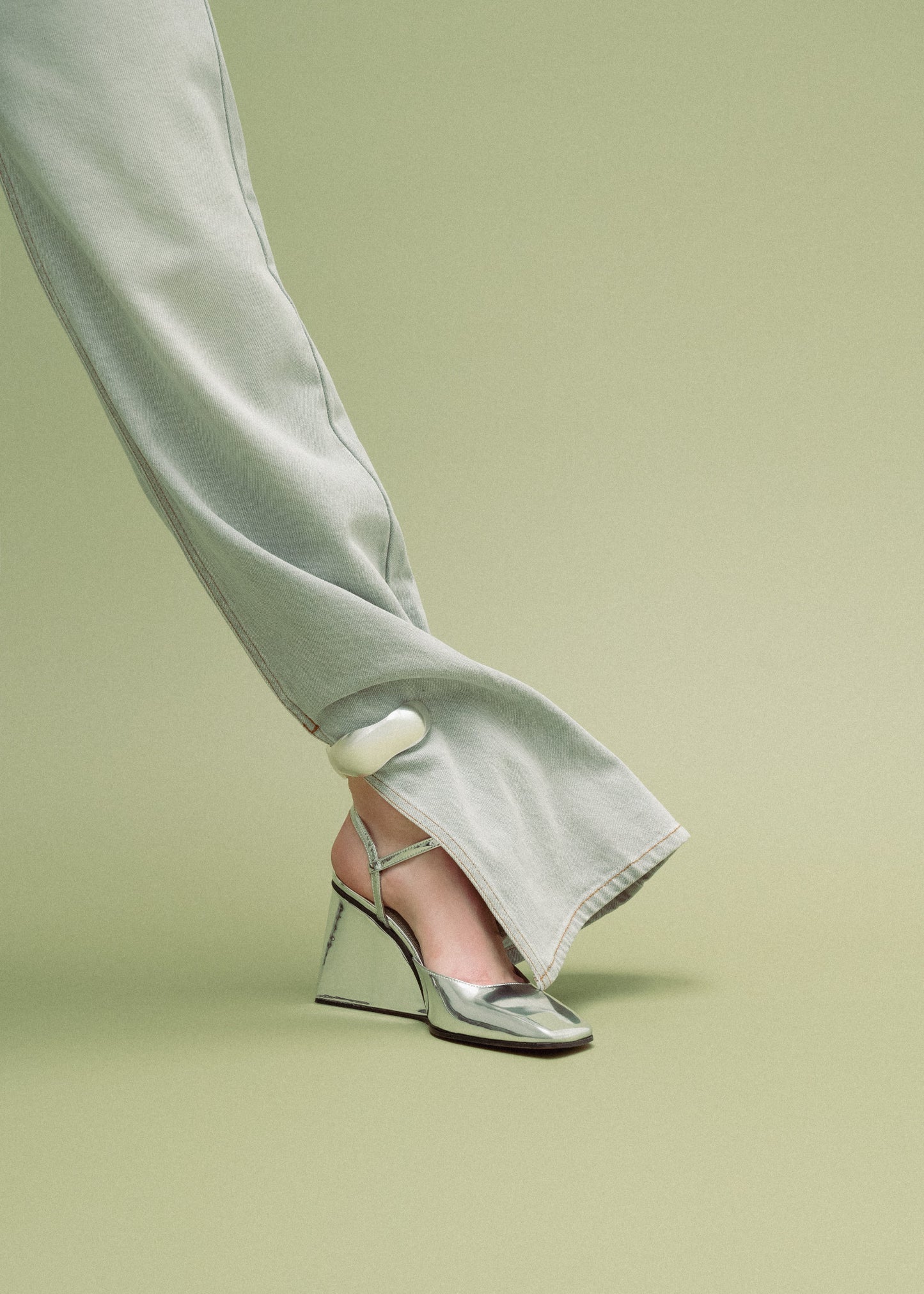 Silver high-heeled shoes worn with light-colored pants on a green background