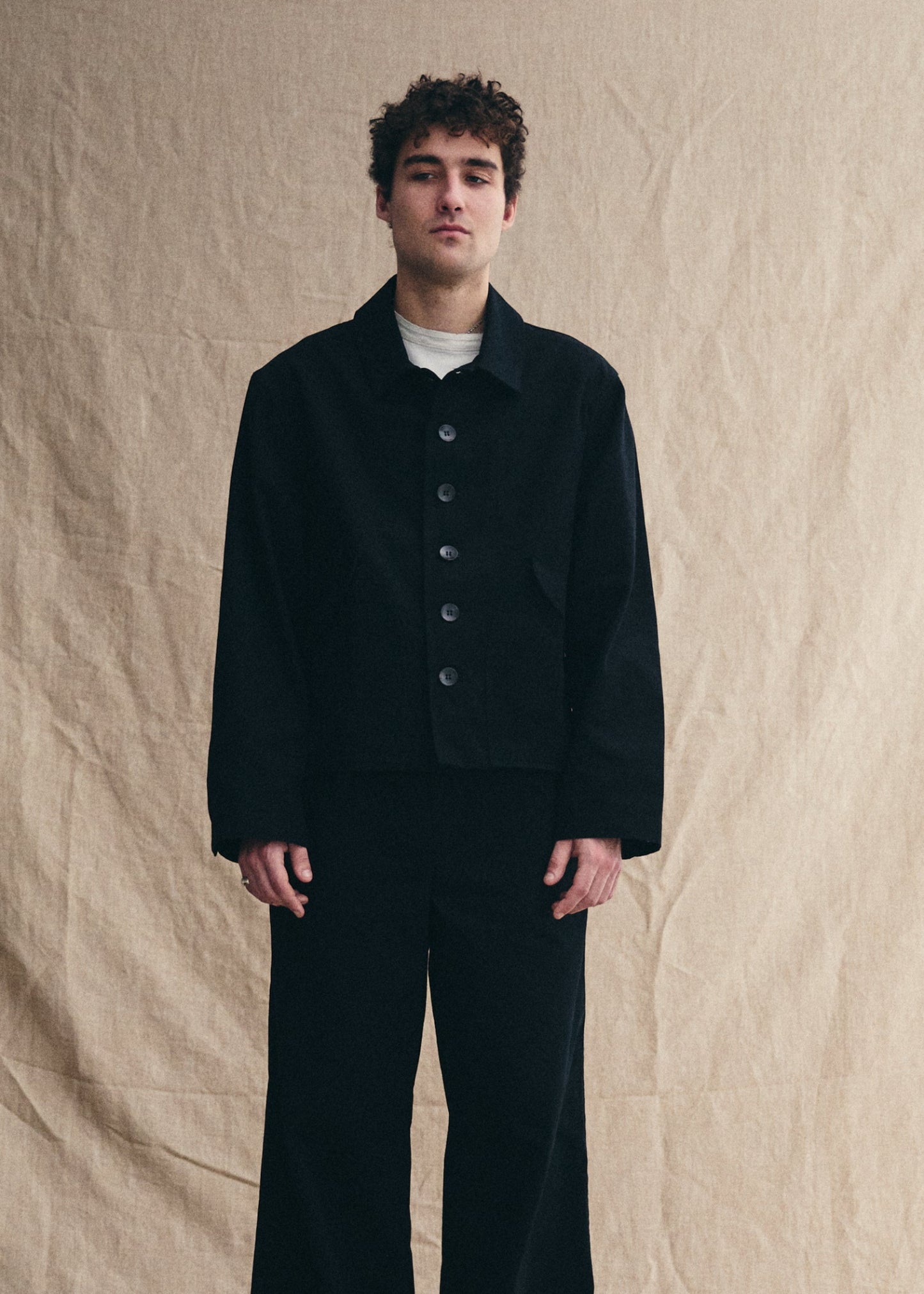 Man wearing a black outfit against a beige background