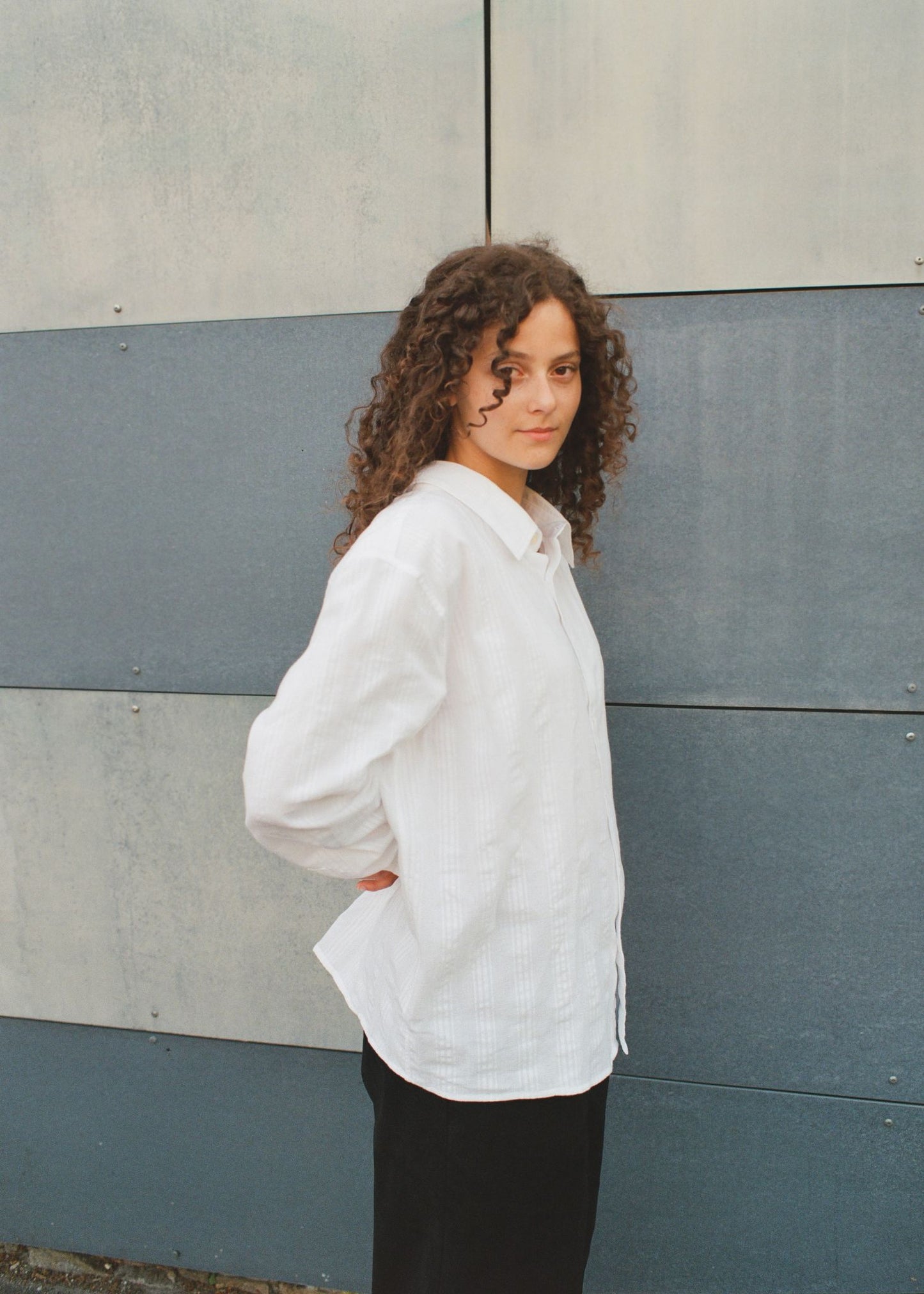 Person wearing a white shirt standing against a gray wall