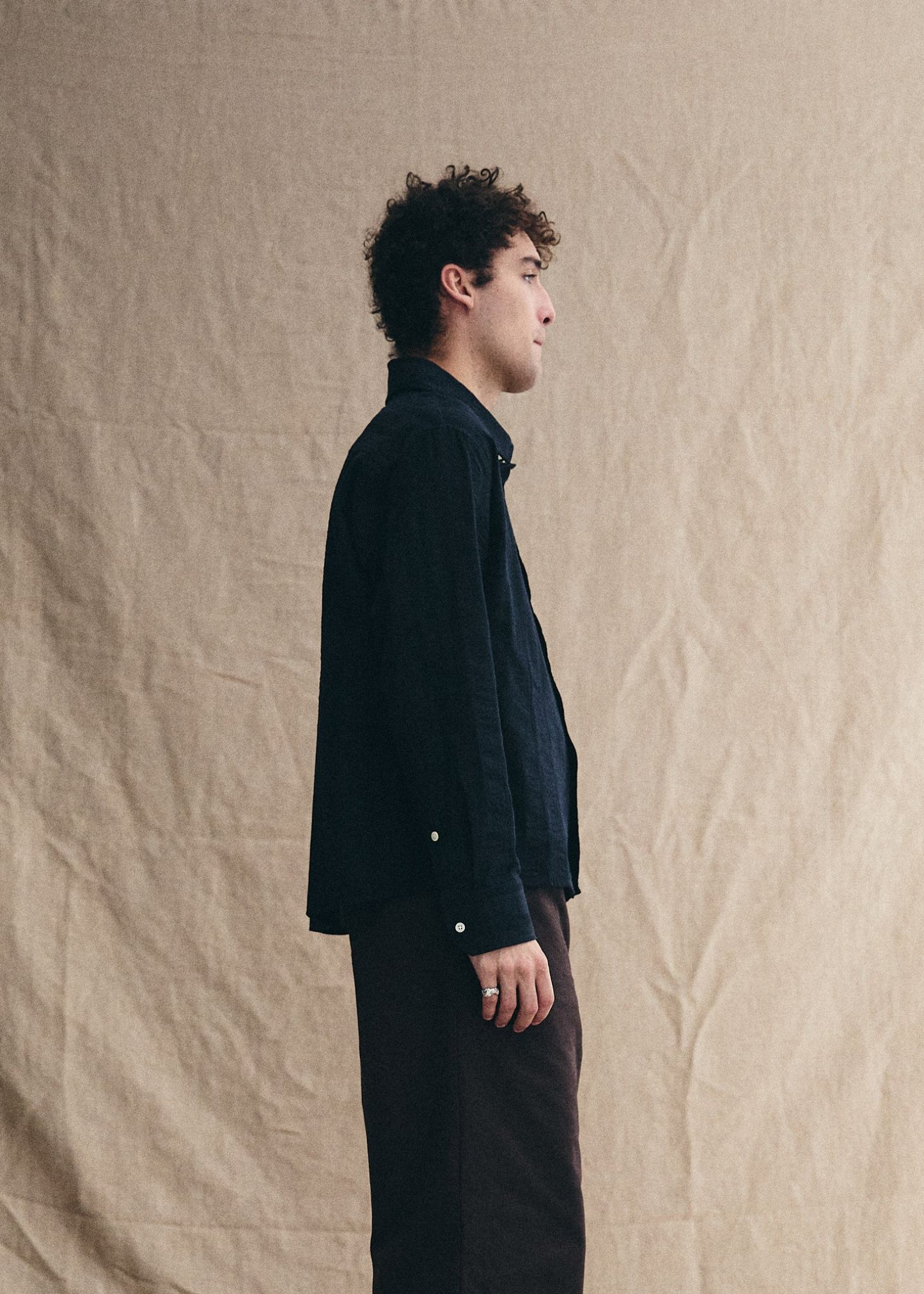 Man wearing a dark jacket and pants standing against a beige textured wall