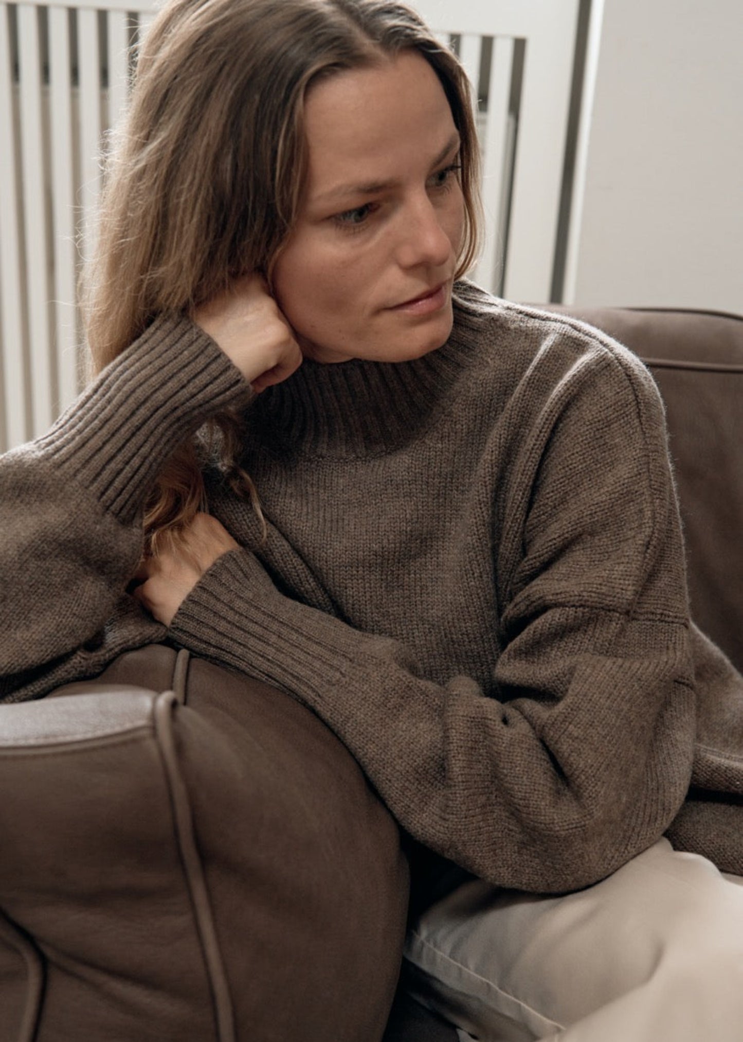 Woman sitting on a couch wearing a brown sweater.