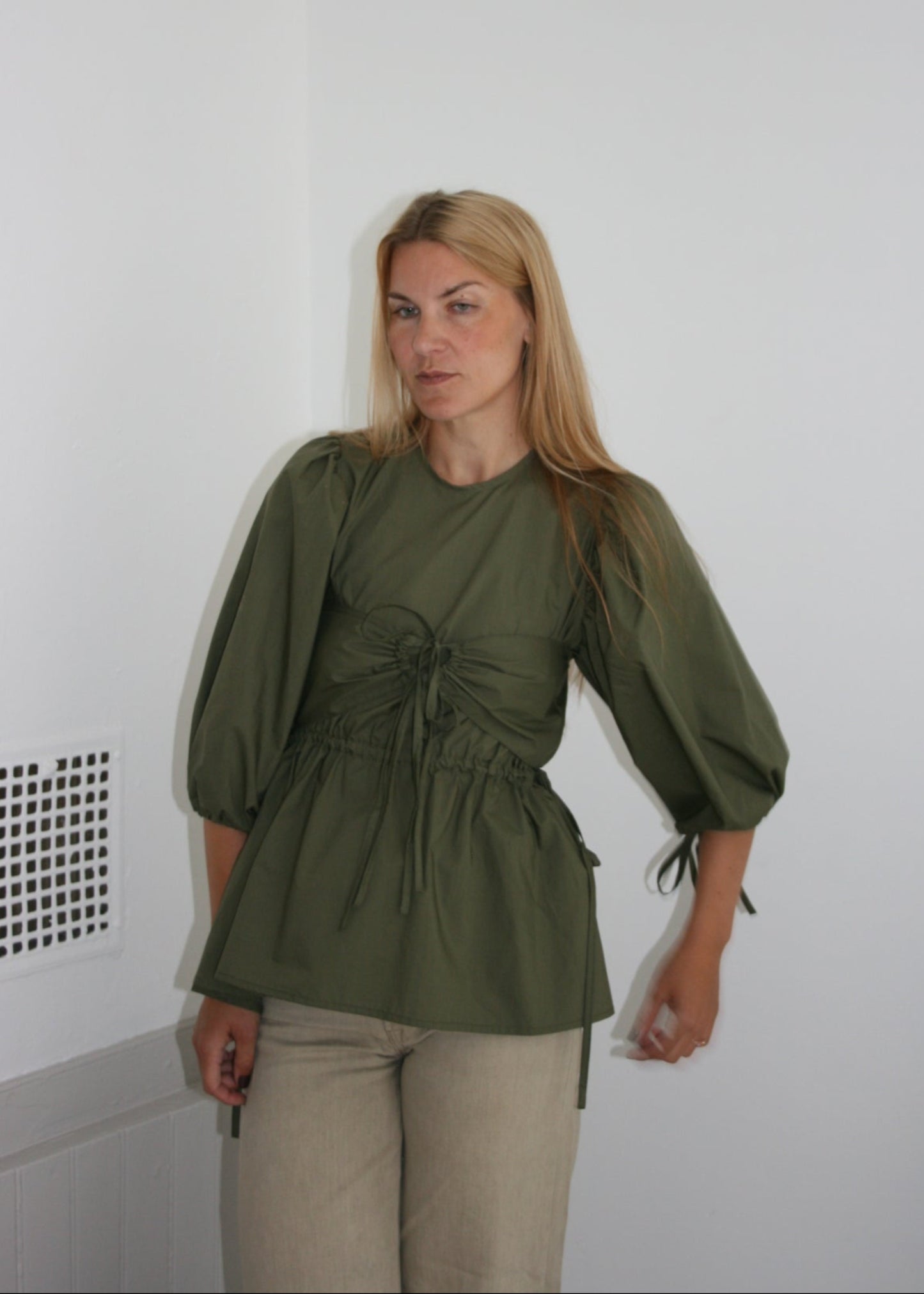 Woman wearing a green blouse and beige pants on a white floor.
