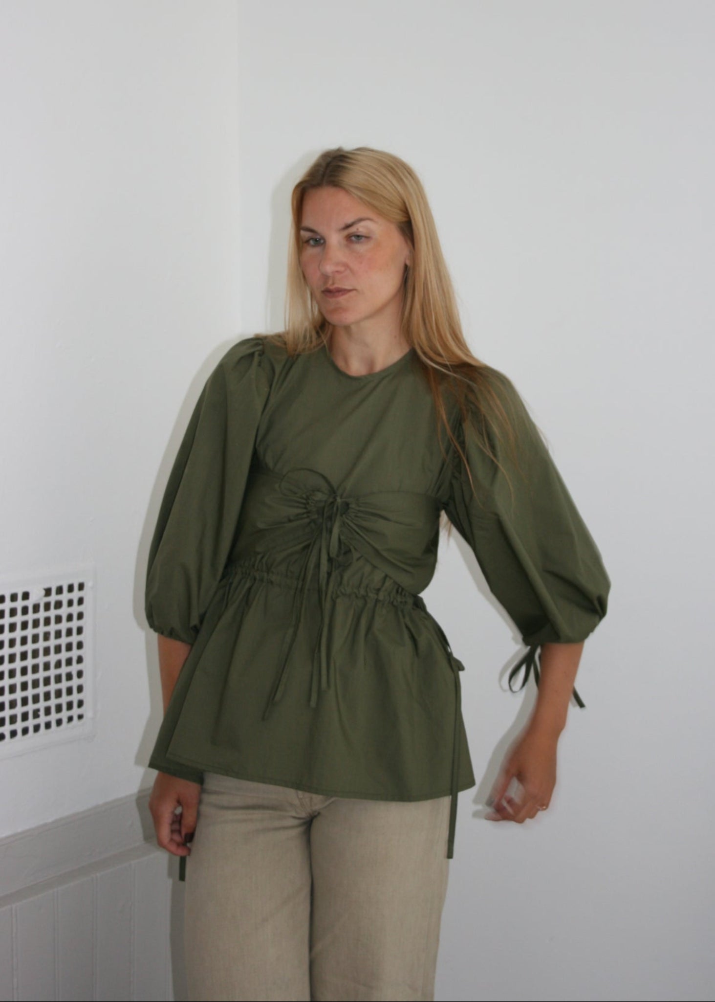 Woman wearing a green blouse and beige pants on a white floor.
