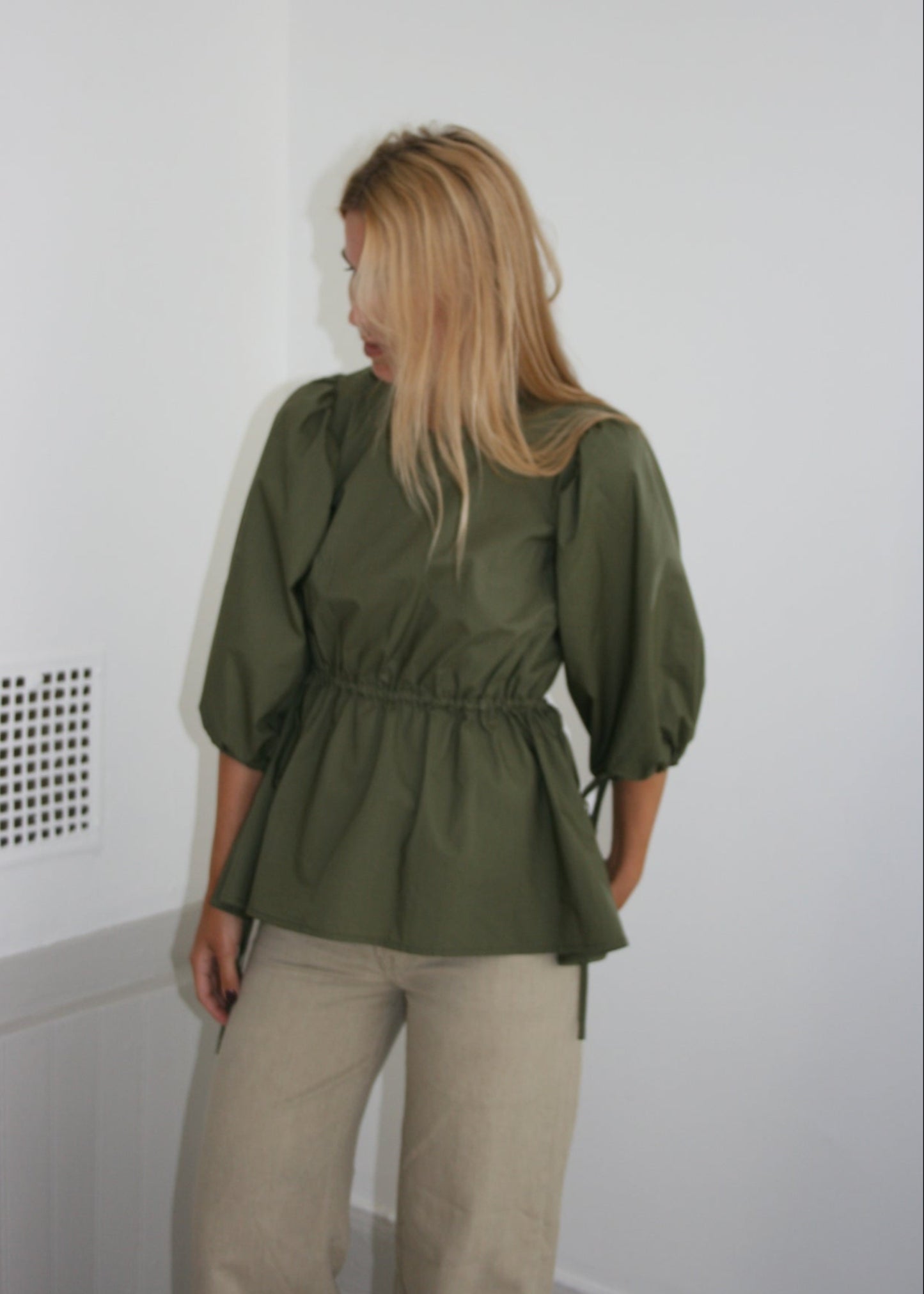 Person wearing a green blouse on a white floor with a light gray wall.