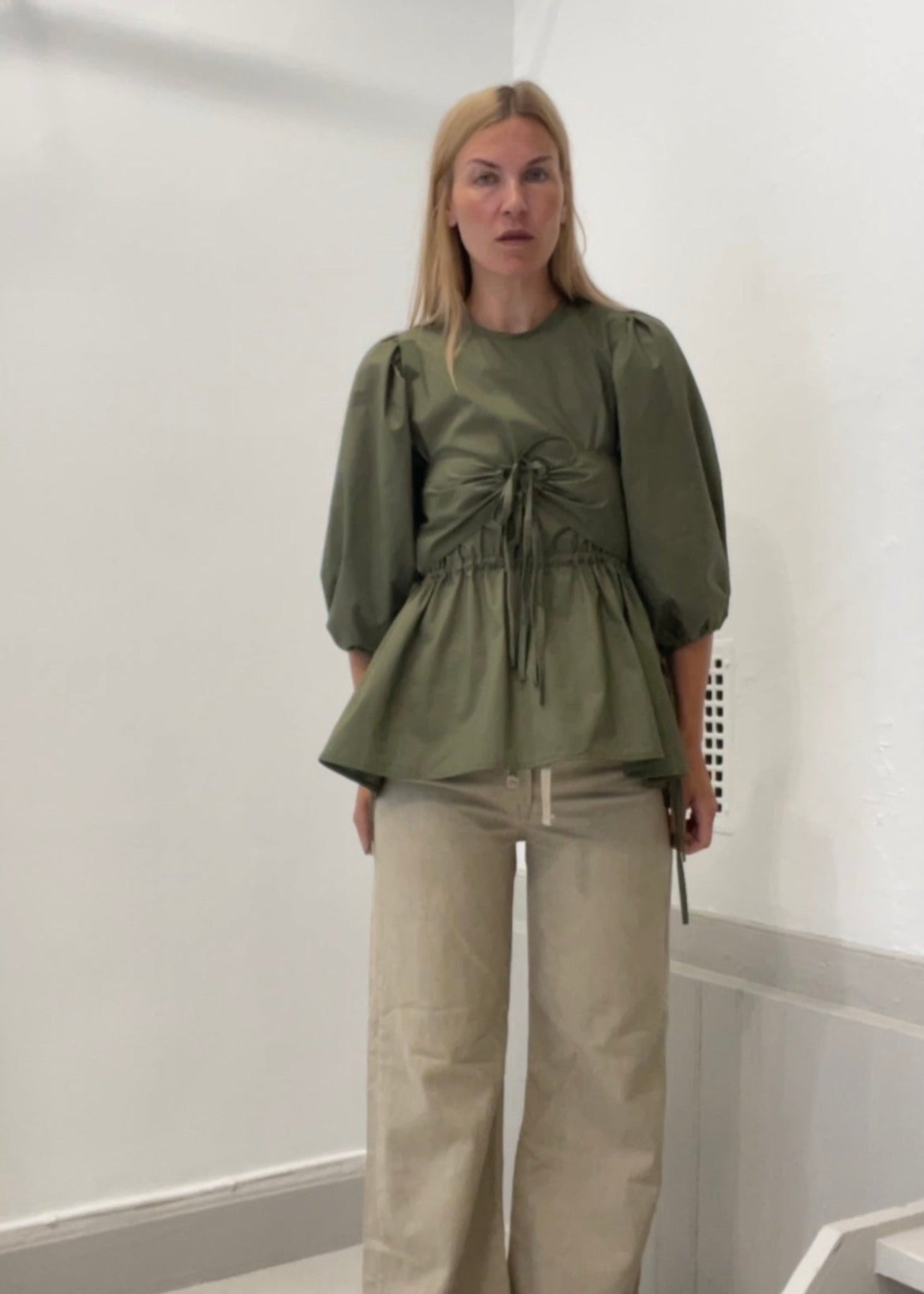 Woman wearing a green top and beige pants standing in a bathroom.