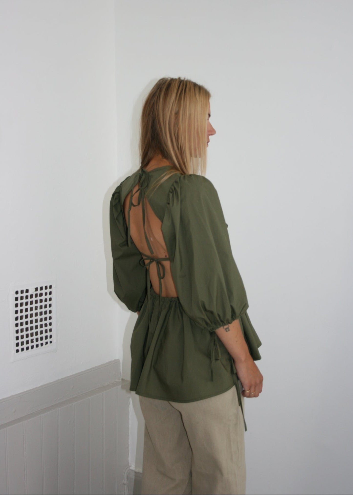 Person wearing a green blouse and beige pants on a white floor.