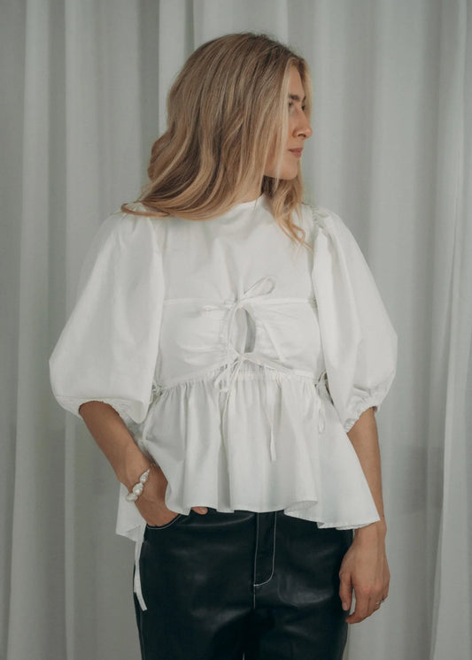 Woman wearing a white blouse with puffed sleeves against a plain background
