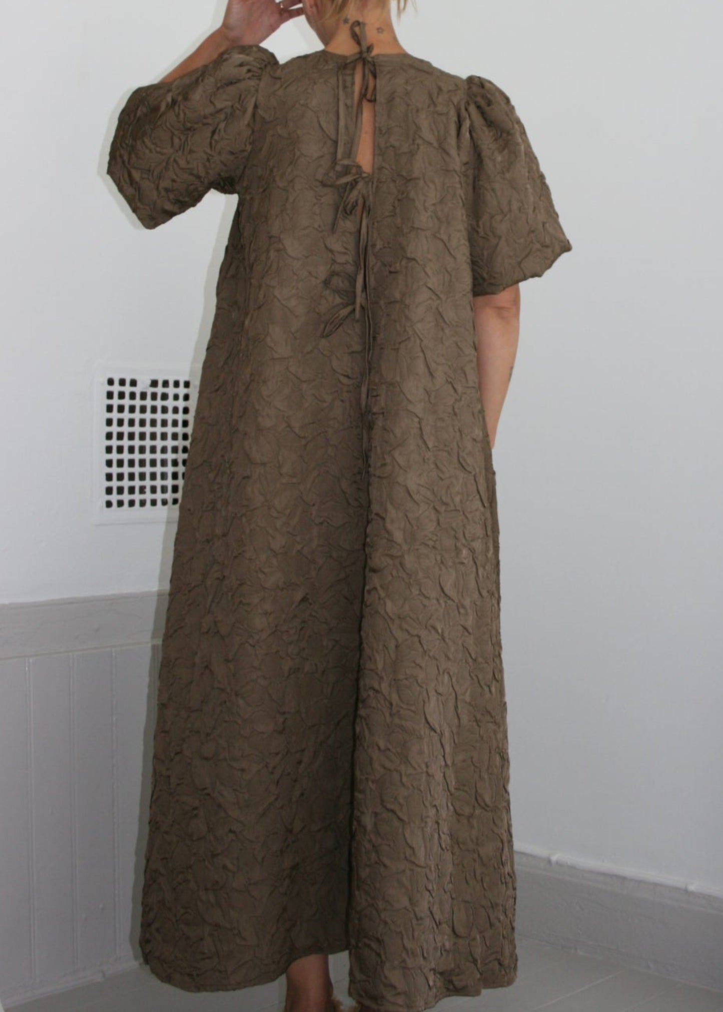 Person wearing a long brown dress in a minimal indoor setting