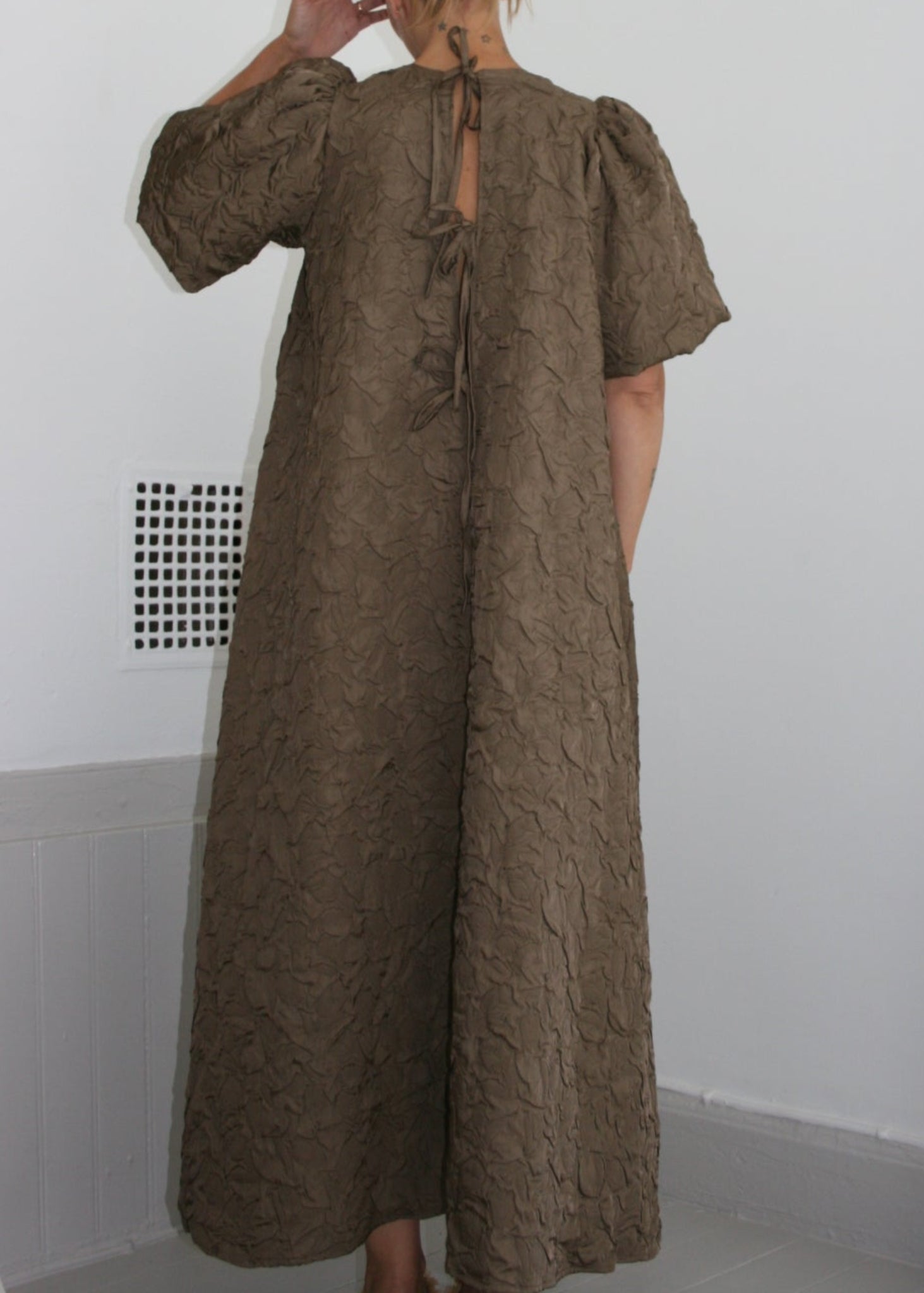Person wearing a long brown dress in a minimal indoor setting