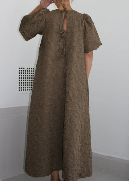 Person wearing a long brown dress in a minimal indoor setting