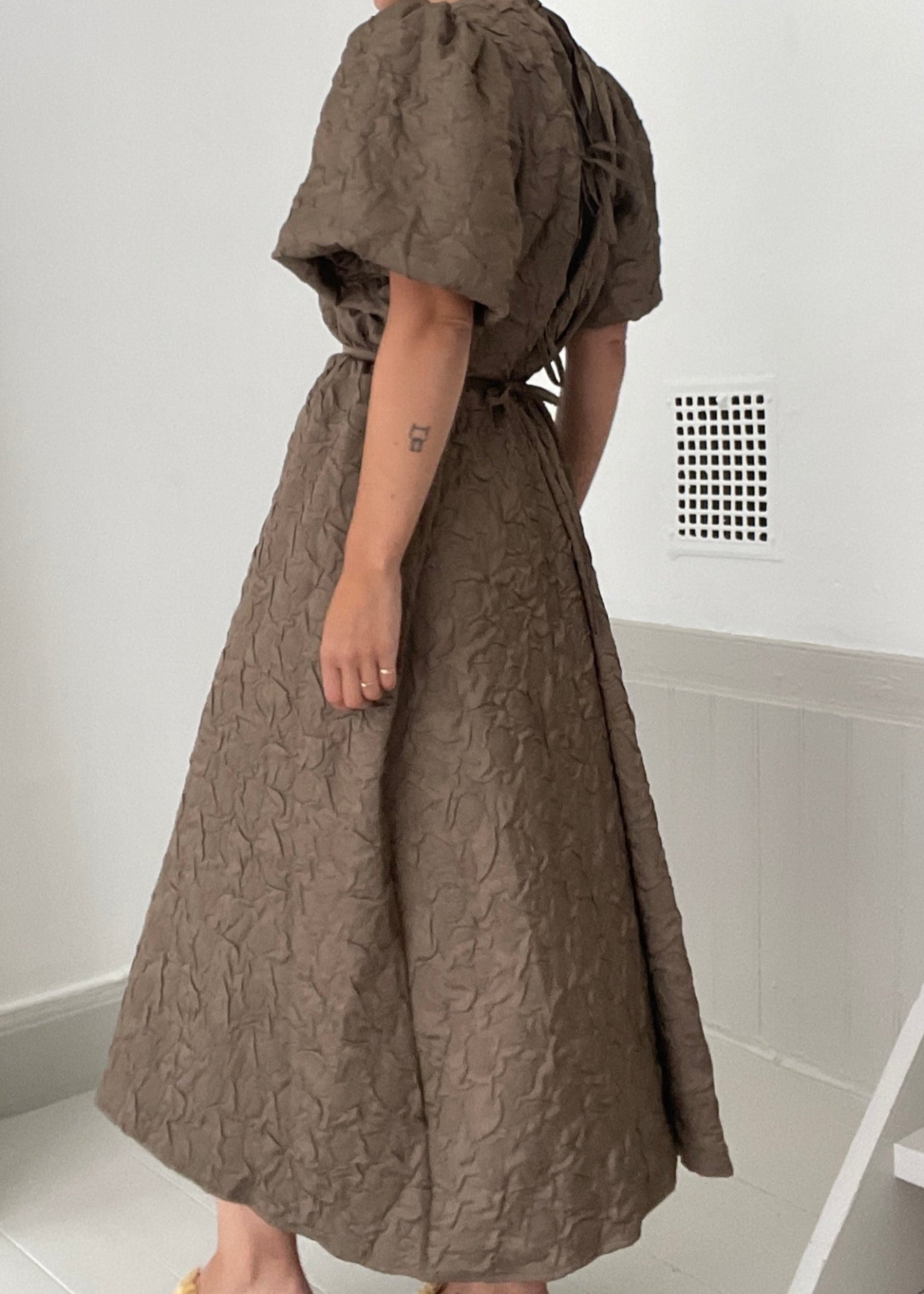 Woman wearing a brown dress in a minimal indoor setting