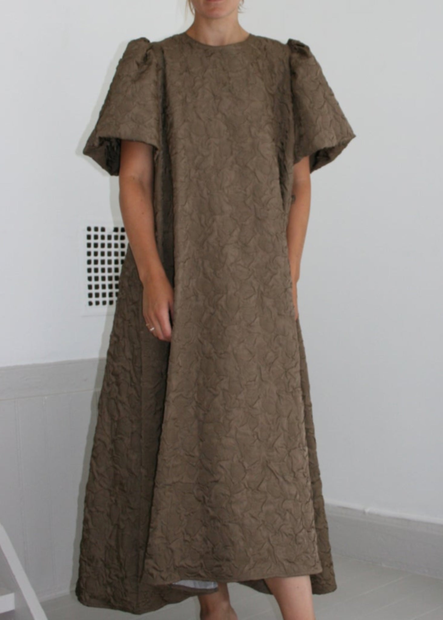 Person wearing a brown dress standing in front of a mirror on a white floor.