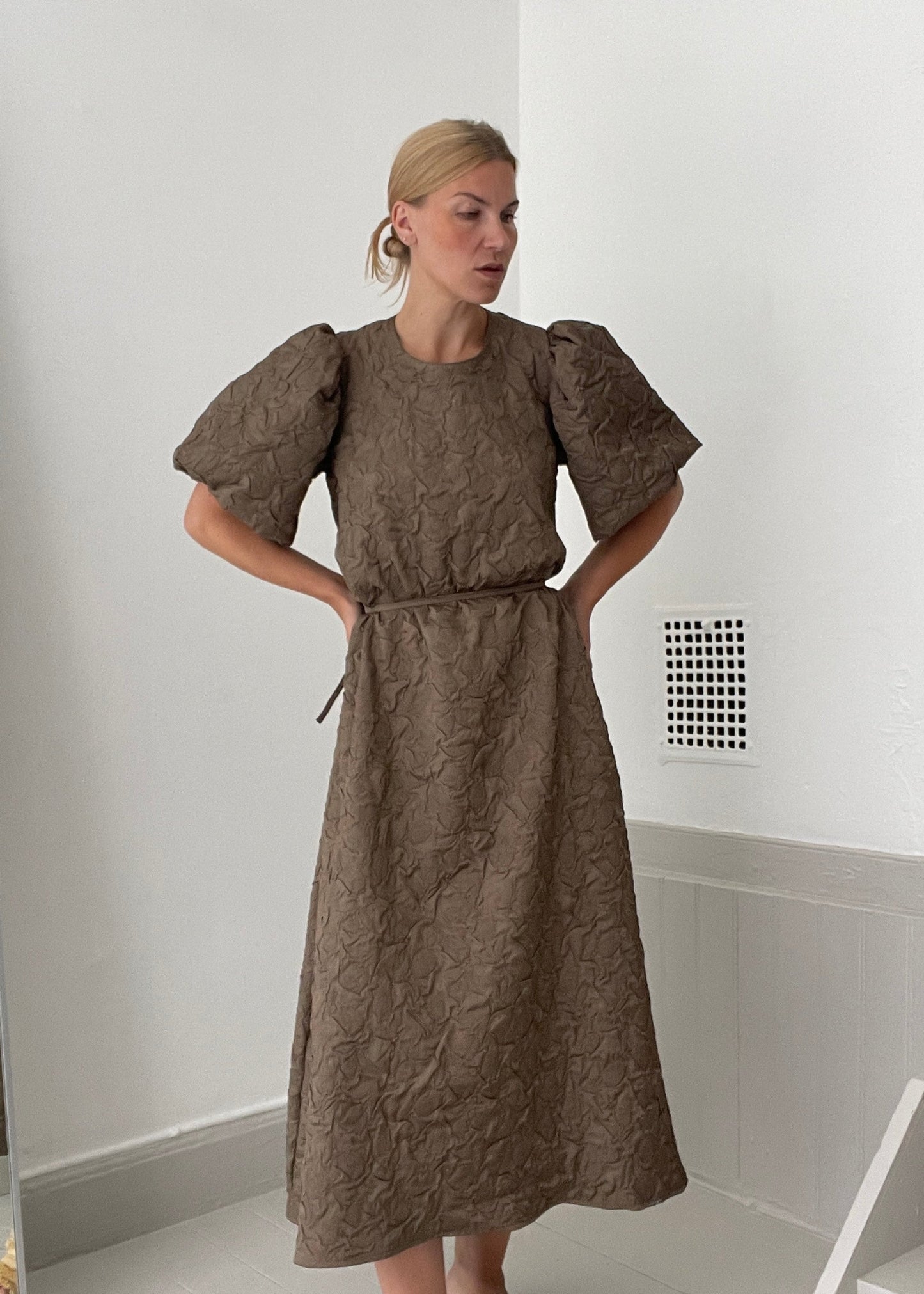 Woman wearing a brown dress in a minimal white room