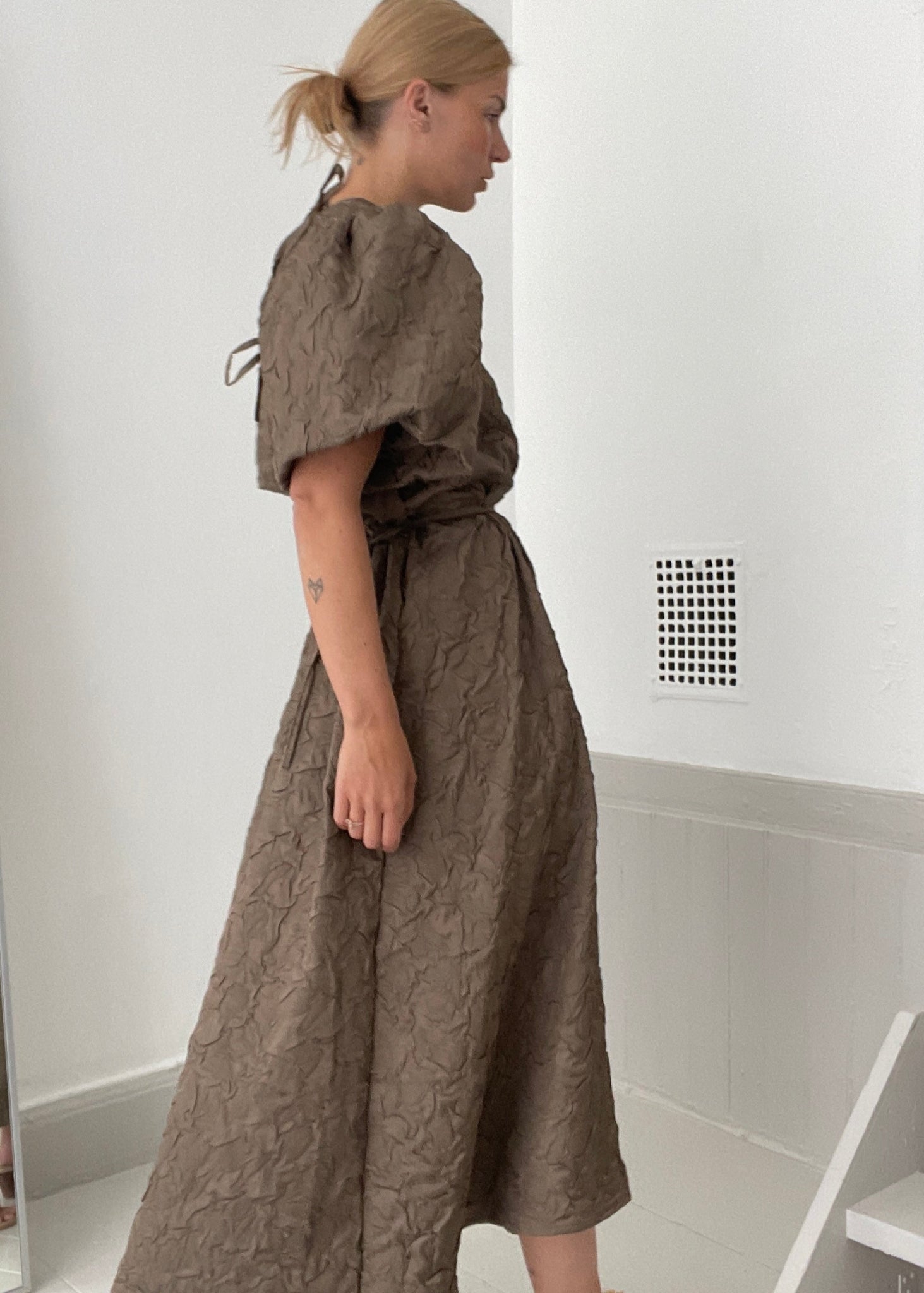 Woman wearing a brown textured dress in a minimal indoor setting