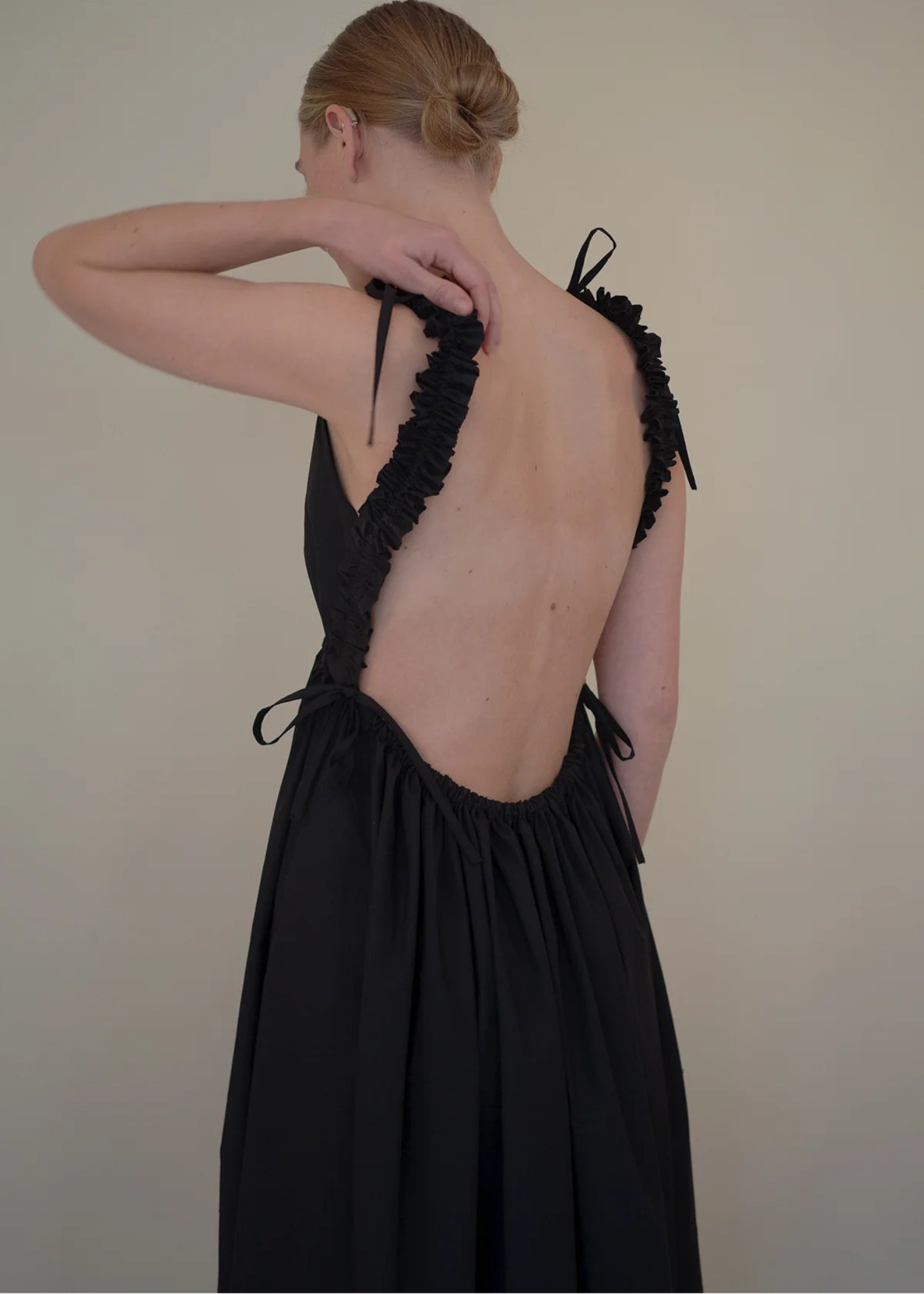 Woman wearing a black dress with open back against a plain background