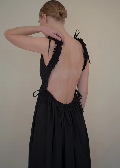 Woman wearing a black dress with open back against a plain background