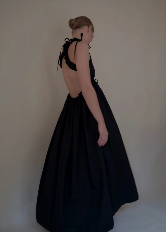 Woman wearing a black dress with open back against a plain background
