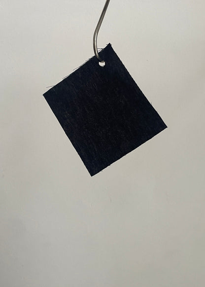 Black square fabric sample hanging on a metal rod against a light gray background
