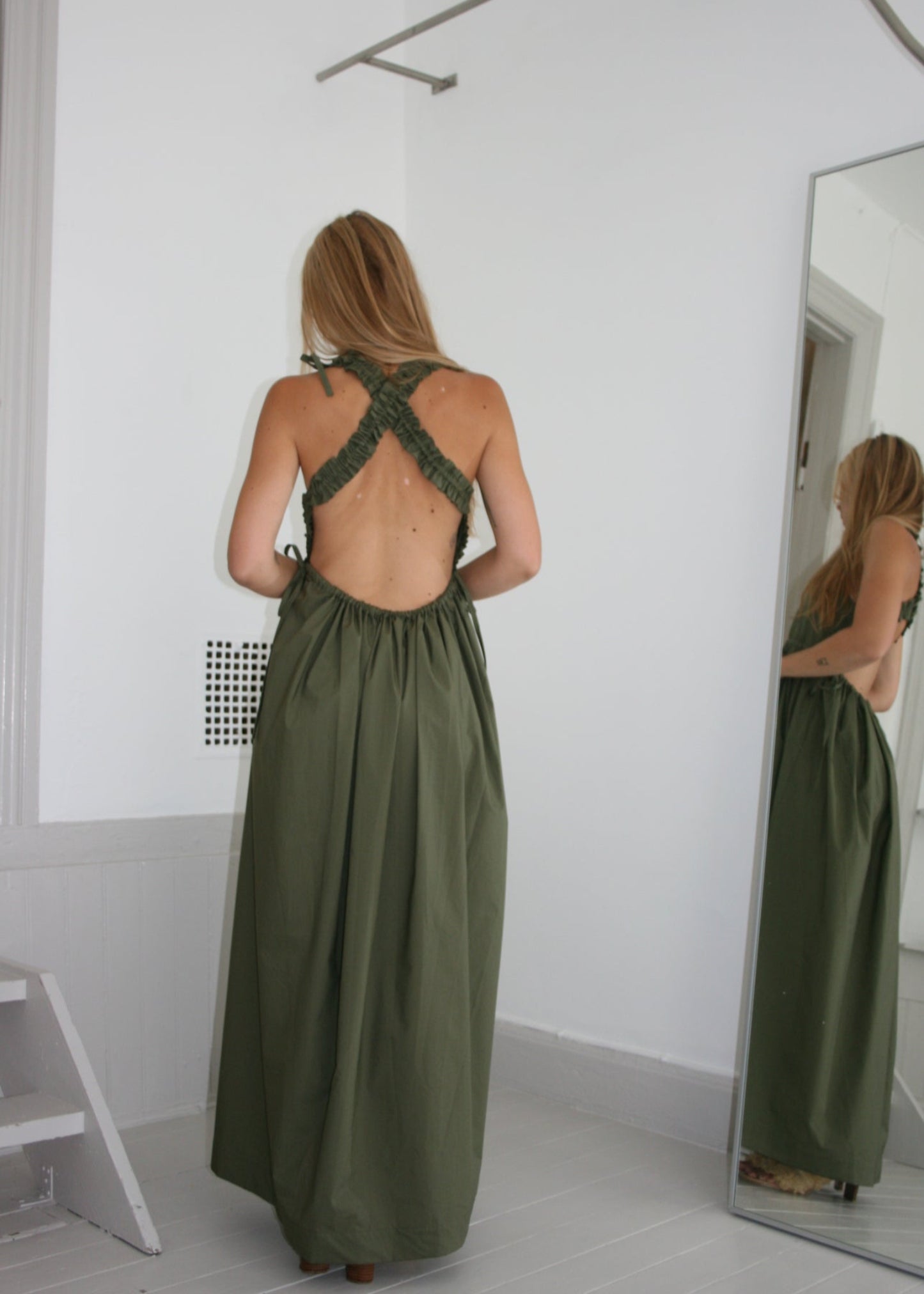 Person wearing a green dress standing on a white floor with a mirror reflecting their back.
