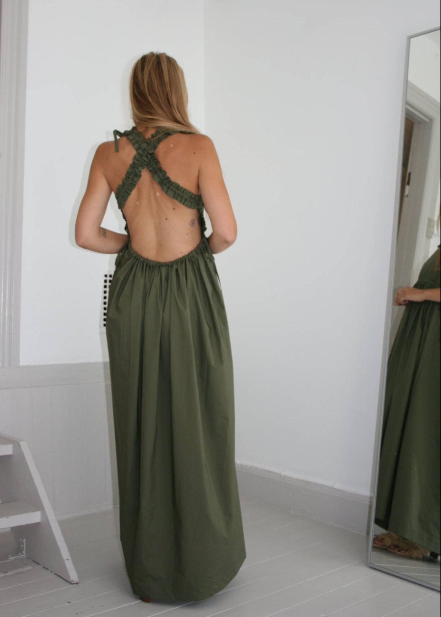 Woman wearing a green dress standing in front of a mirror.