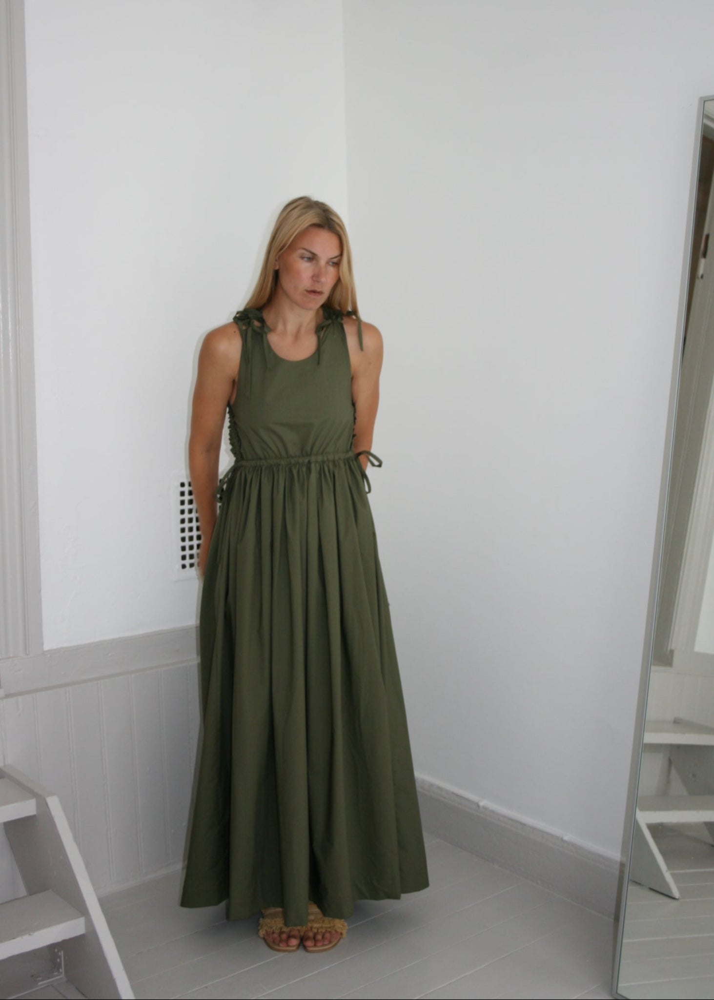 Woman wearing a green dress standing in a room with white walls and a door.