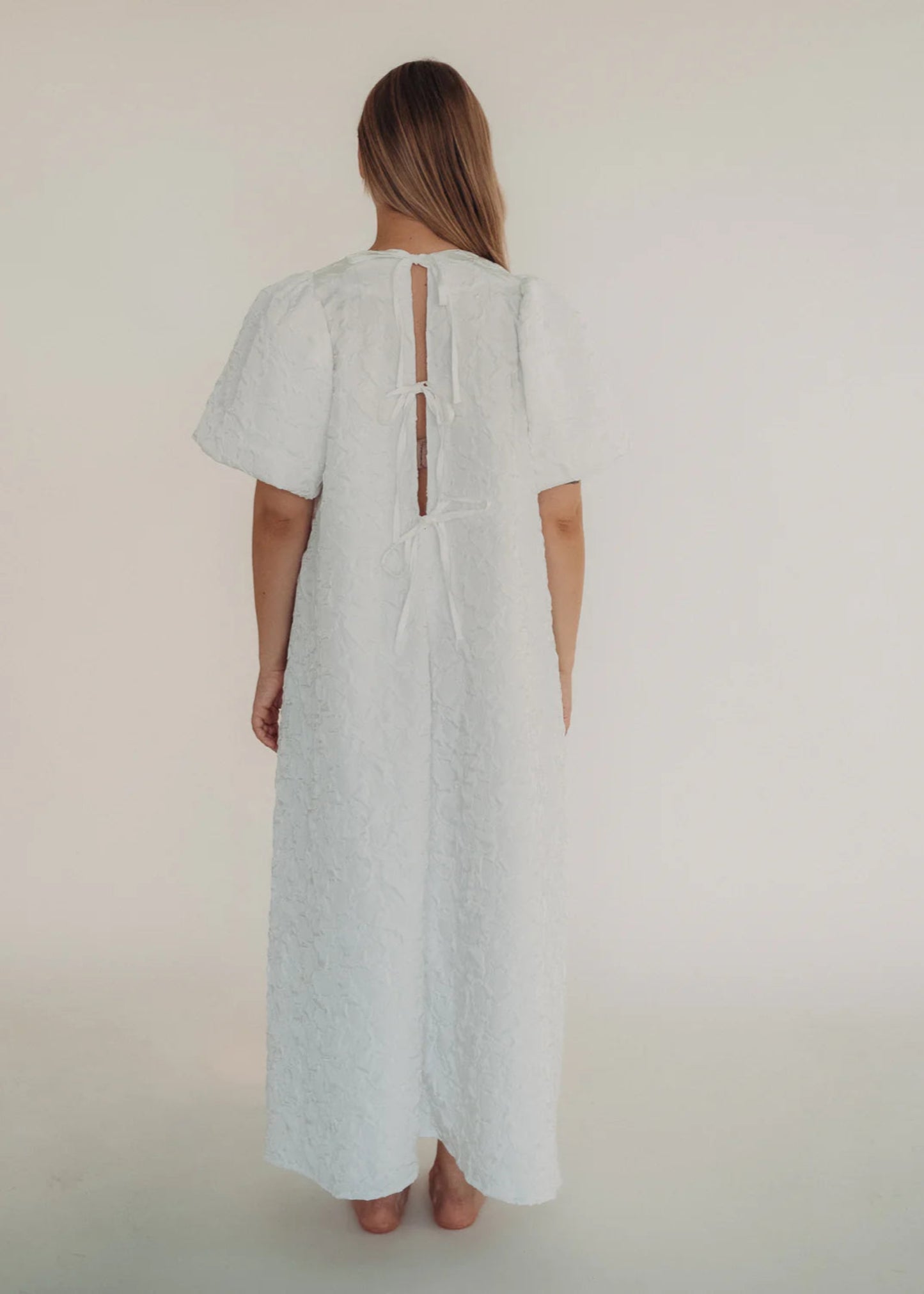 Woman wearing a white dress with a cut-out back design on a plain background
