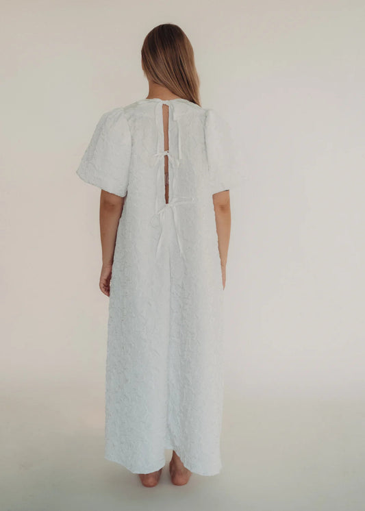 Woman wearing a white dress with a cut-out back design on a plain background