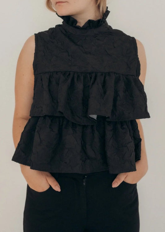 Woman wearing a black sleeveless ruffled top against a plain background
