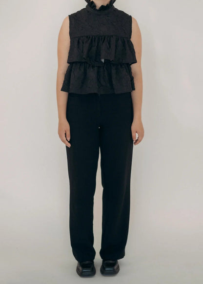 Person wearing a black sleeveless ruffled top and black pants on a white background