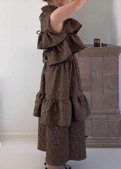 Woman in a brown ruffled dress standing in front of a mirror.