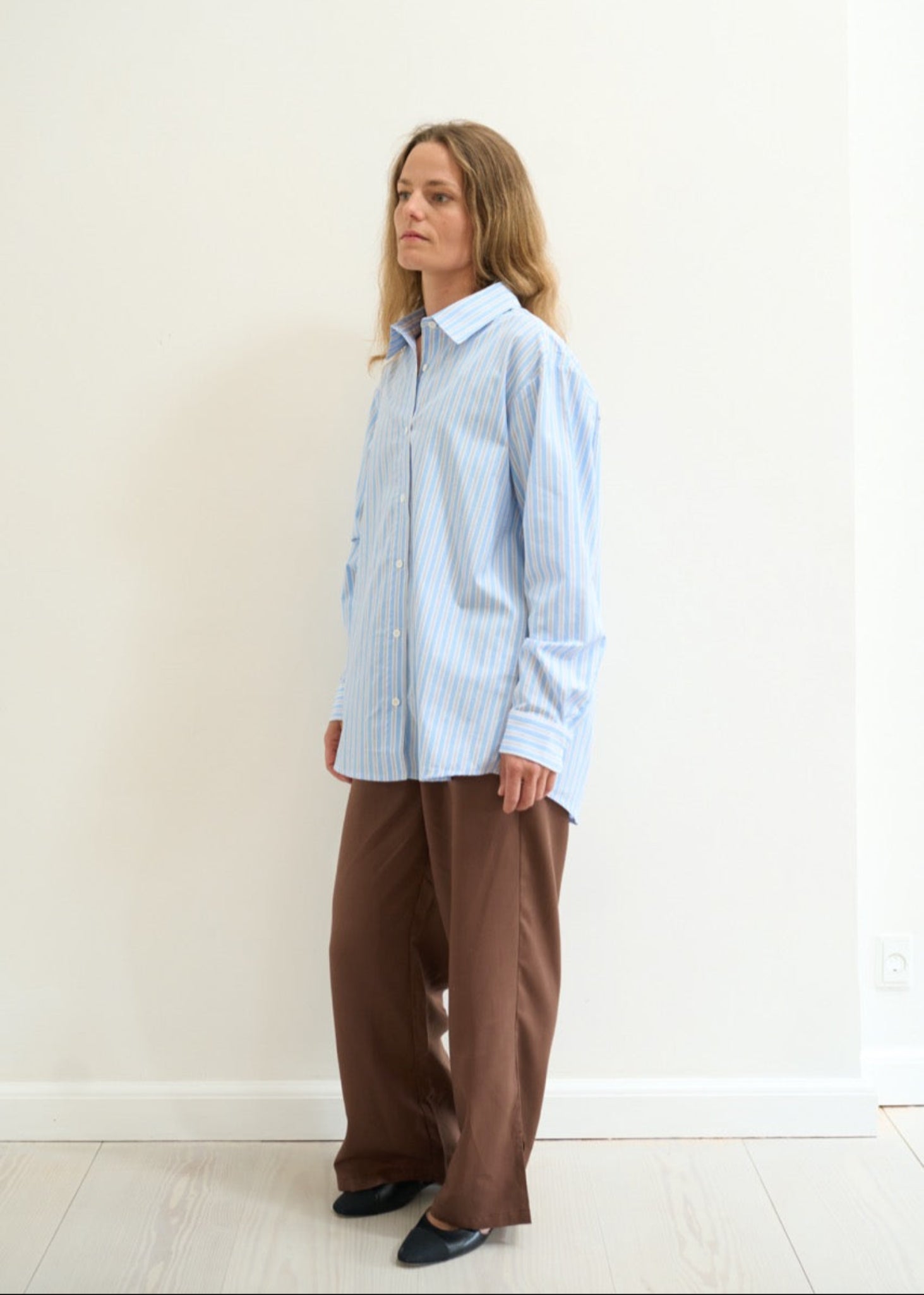 Person wearing a light blue striped shirt and brown pants against a white background
