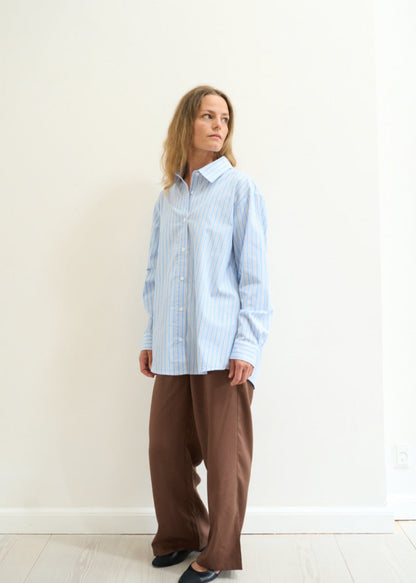Person wearing a light blue checkered shirt and brown pants against a white background