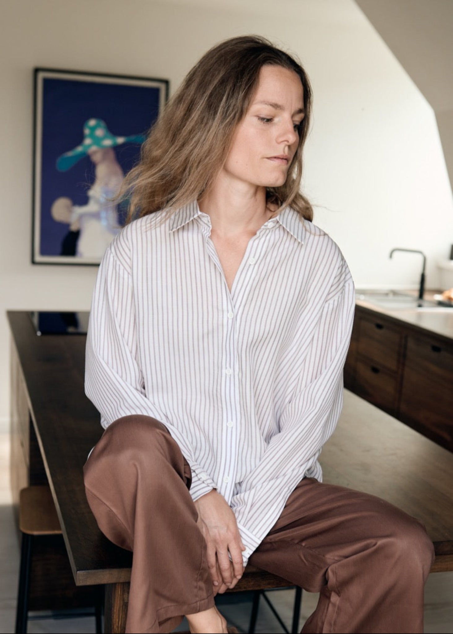 Woman sitting on a bench in a room with a painting on the wall.