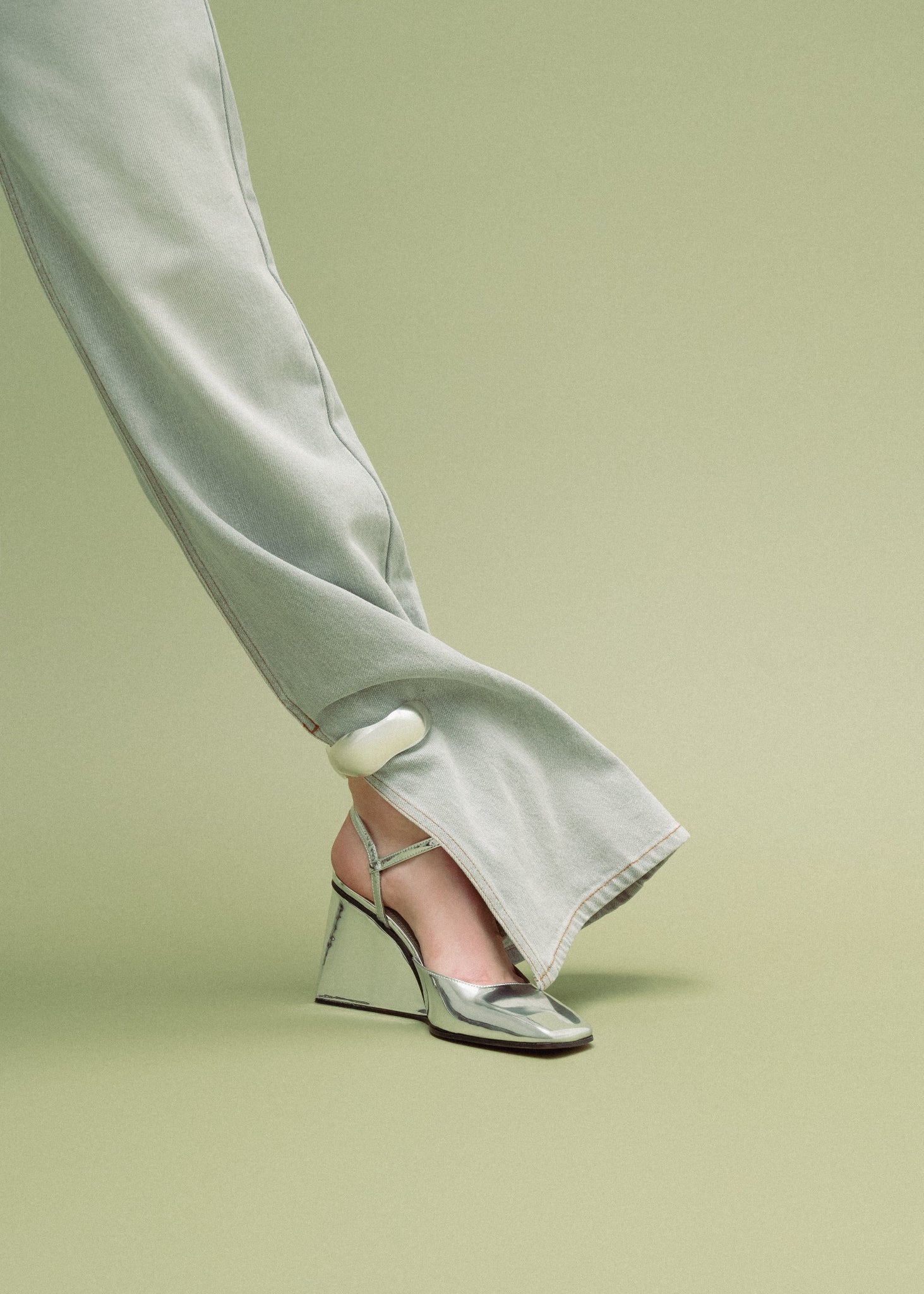 Silver high-heeled shoes worn with light-colored pants on a green background