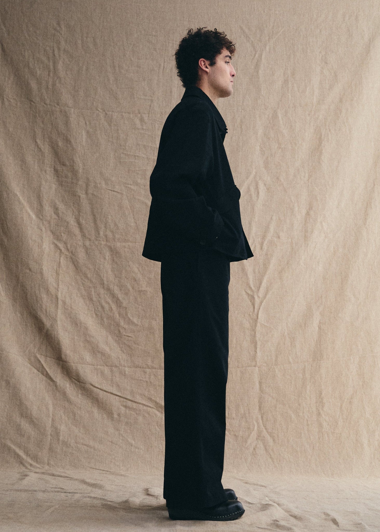 Person wearing a black suit standing against a beige background