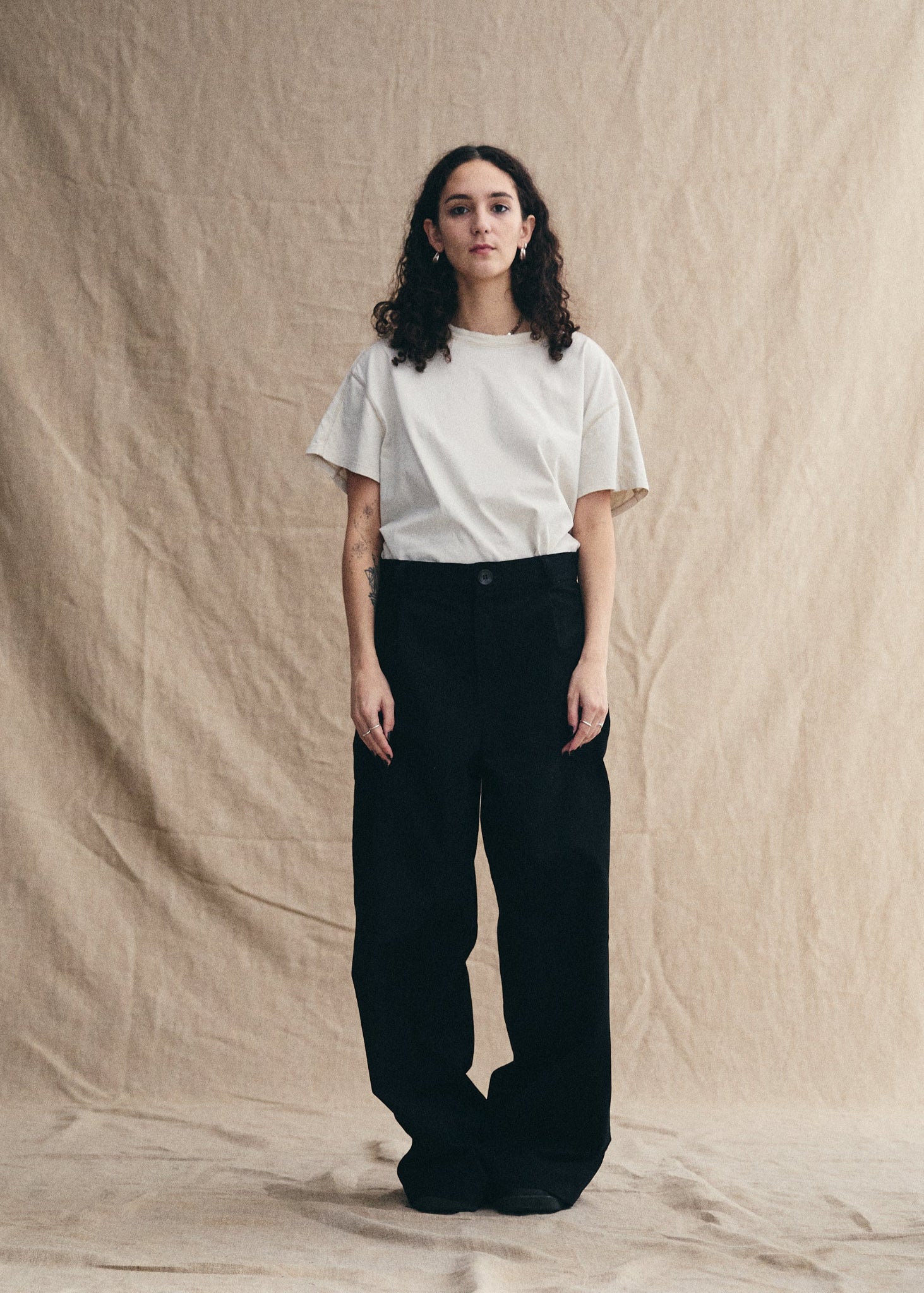 Person wearing a white t-shirt and black pants against a beige background