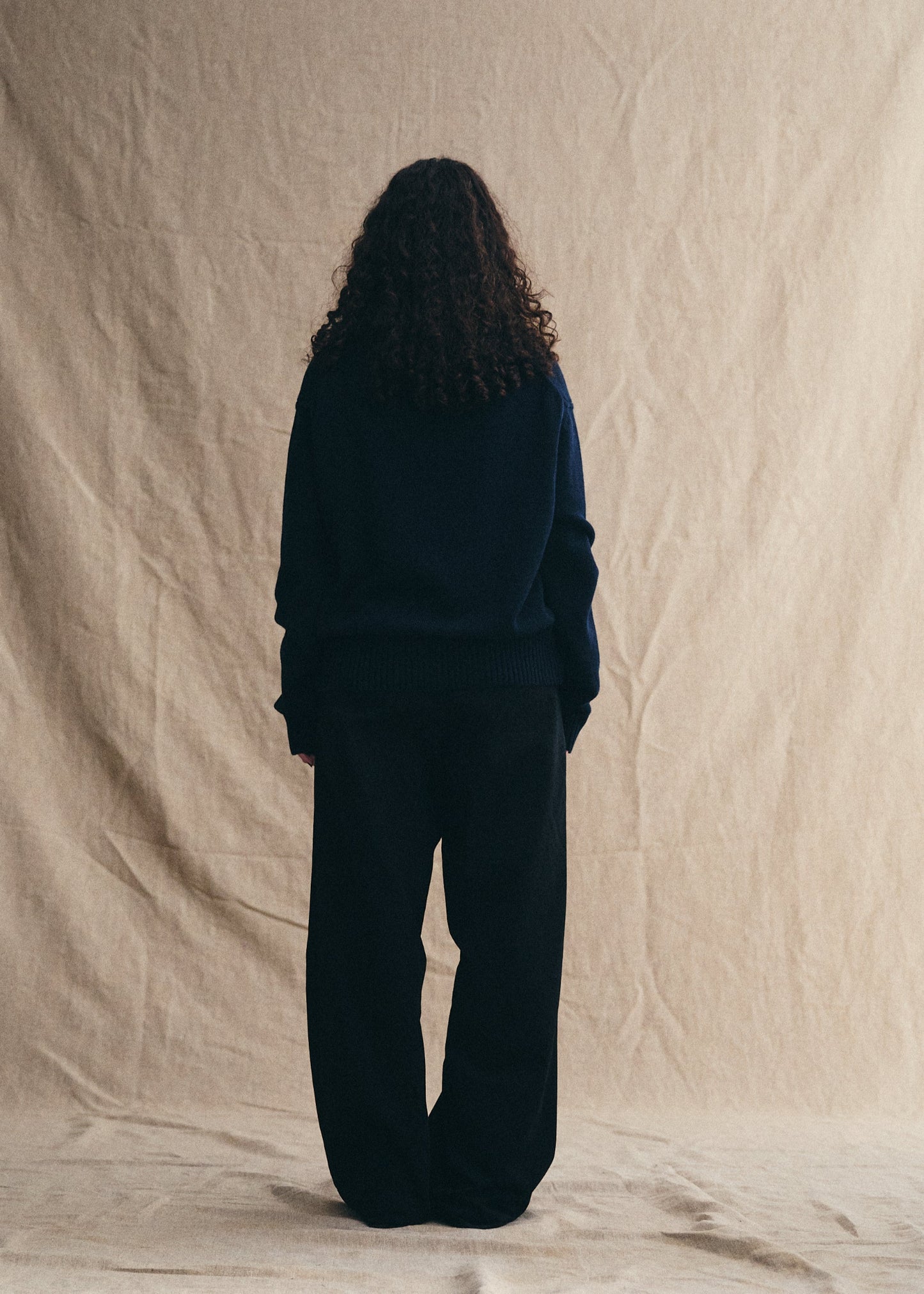 Person wearing a dark outfit standing against a beige backdrop