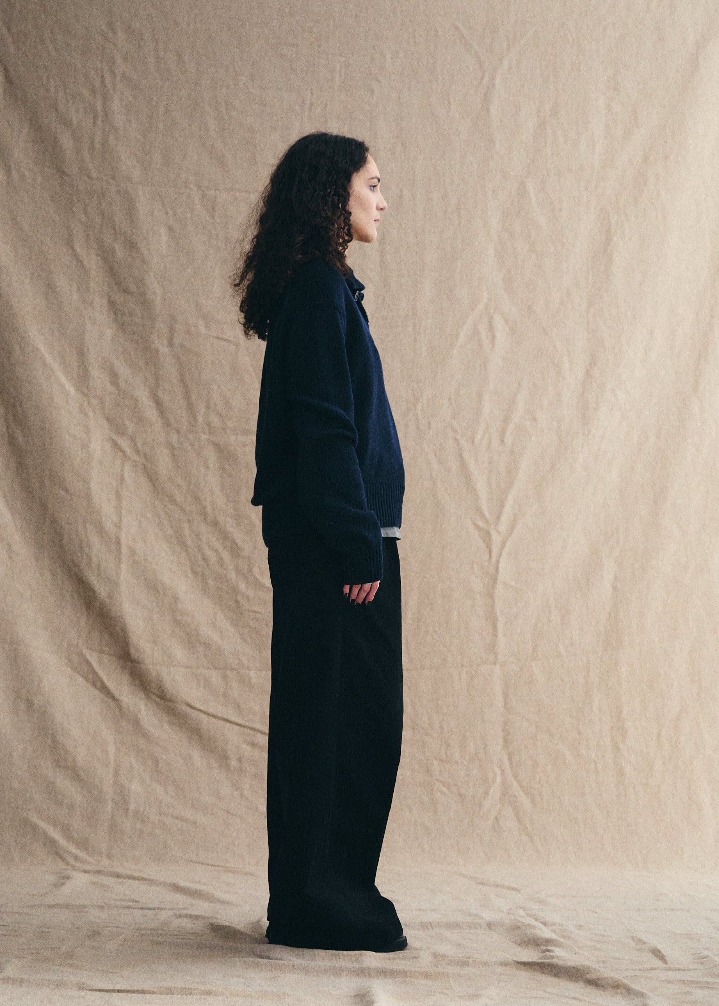 Person wearing a dark outfit standing against a beige backdrop