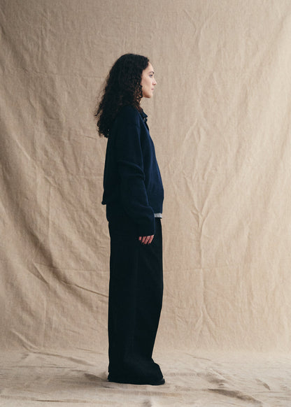 Person wearing a dark outfit standing against a beige backdrop
