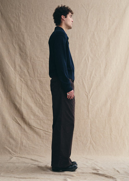 Man standing against a beige backdrop wearing a dark sweater and pants.